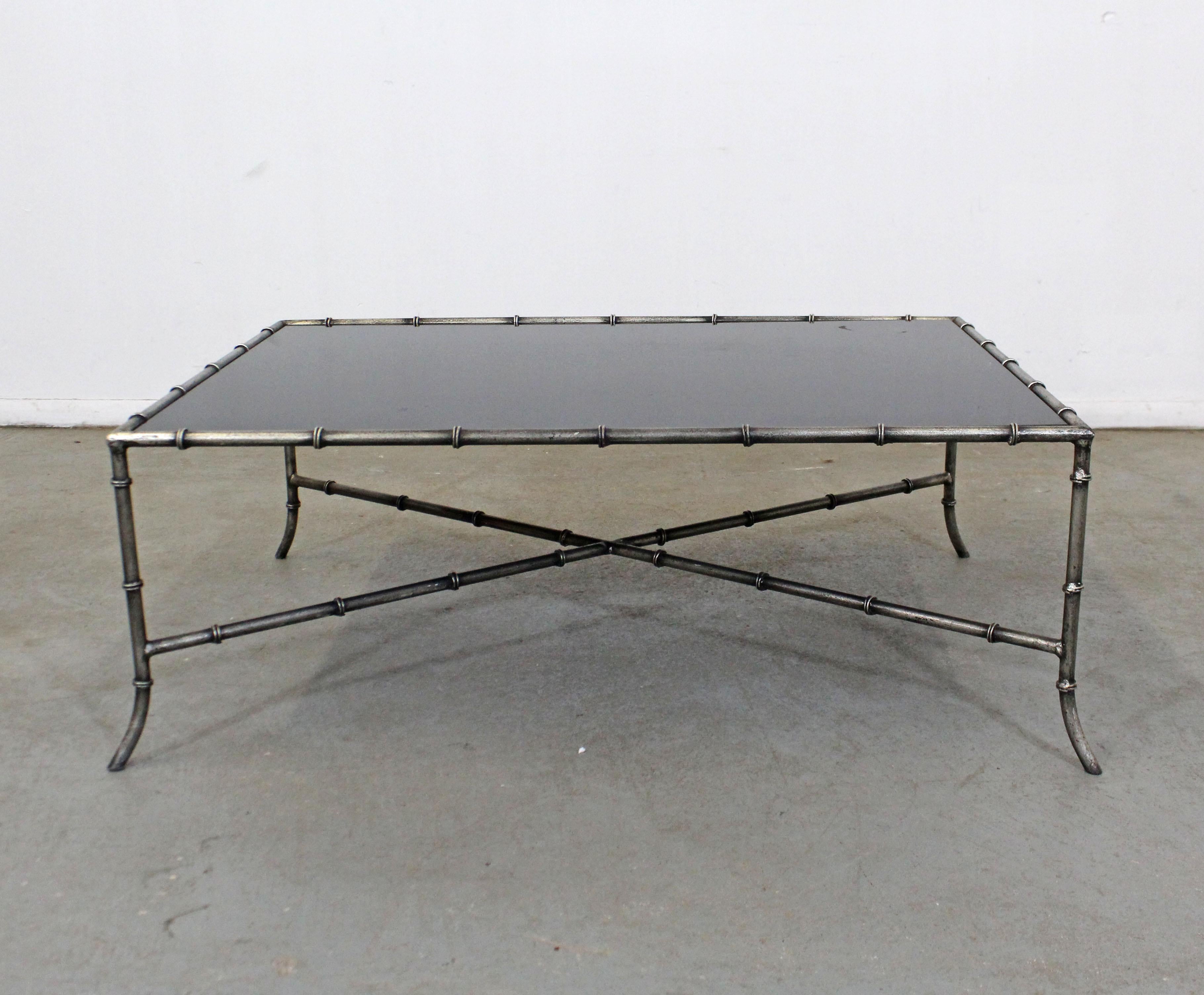 Offered is a vintage iron and glass table similar to the style of Maison Baguès with a faux bamboo look. This table has an iron base with a blacked-out glass top. It is in good structurally sound condition with some cosmetic wear including age wear