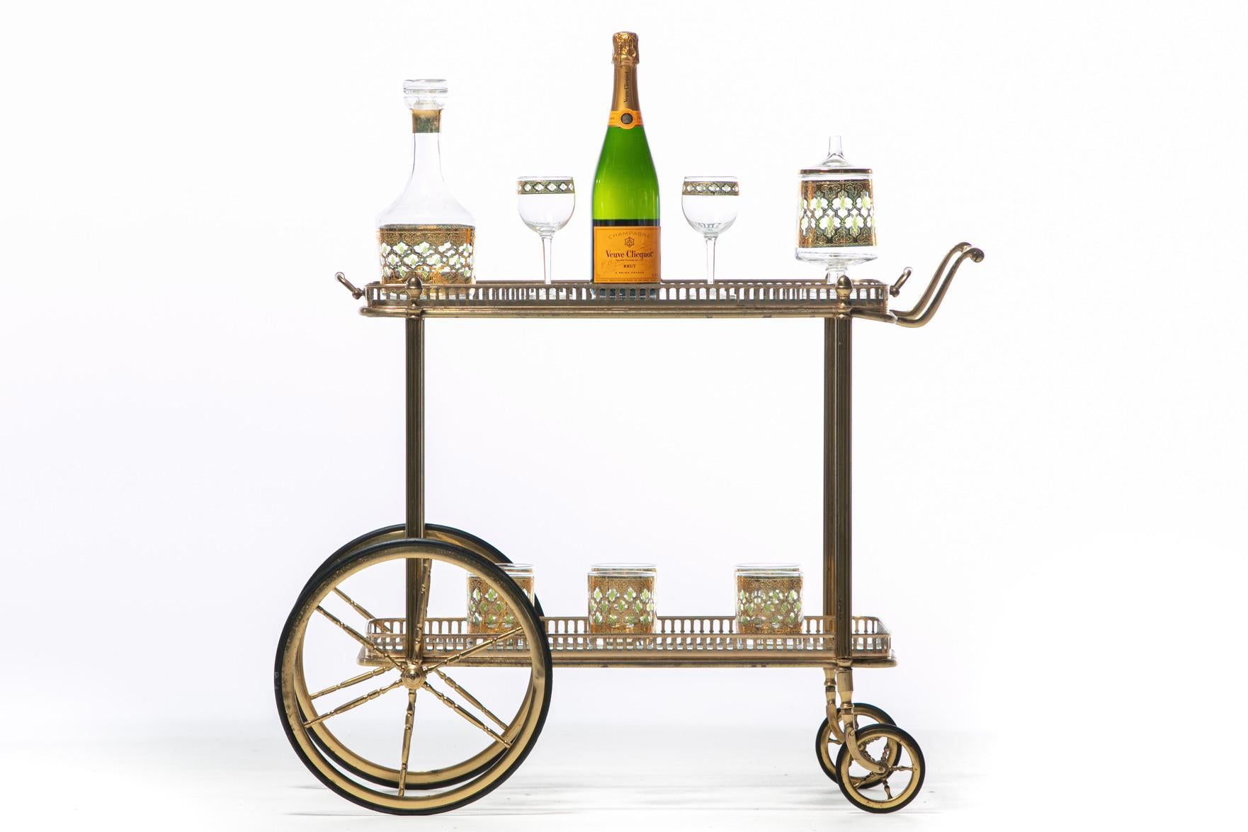 Roll into cocktail hour in style with this chic French neoclassical brass bar cart in the style of Maison Bagués. The details. Two tiers both with glass shelves surrounded by pierced brass galleries. Empirical Roman inspired leg detail. Wheel spoke