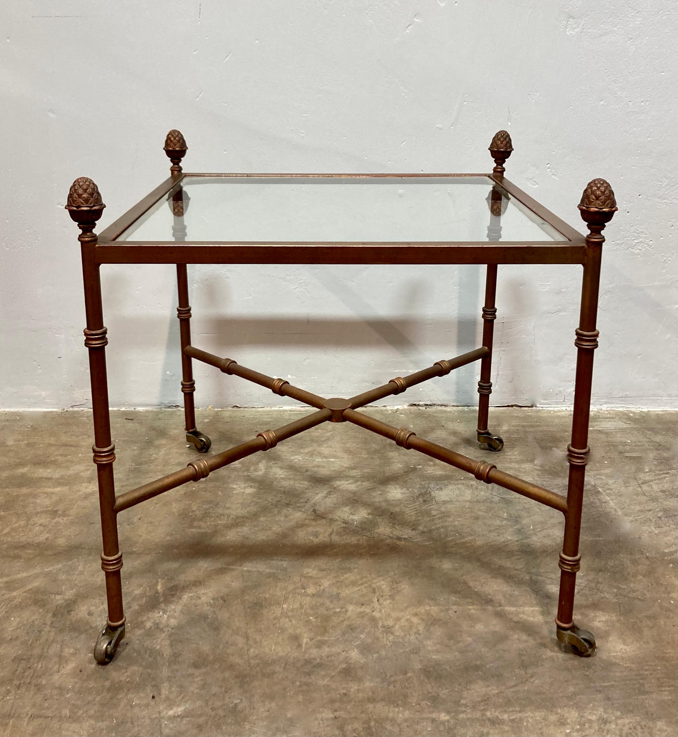 Unique Hollywood Regency style side table, with a brass frame and glass top. Classic faux bamboo frame, much like the style of Maison Bagues. Legs finish in small rolling casters. Each of the four corners are topped with organic sculptural elements.