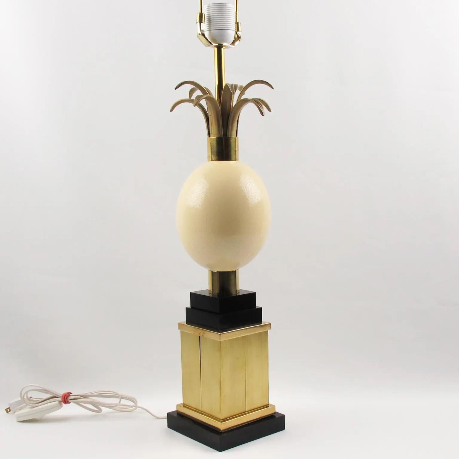 La Maison Charles et Fils, France, a conçu et fabriqué cette jolie lampe de table haute dans les années 1970. La pièce présente un œuf d'autruche massif surmonté de frondes en métal doré sur un socle en laiton doré et en Lucite noire. La lampe est