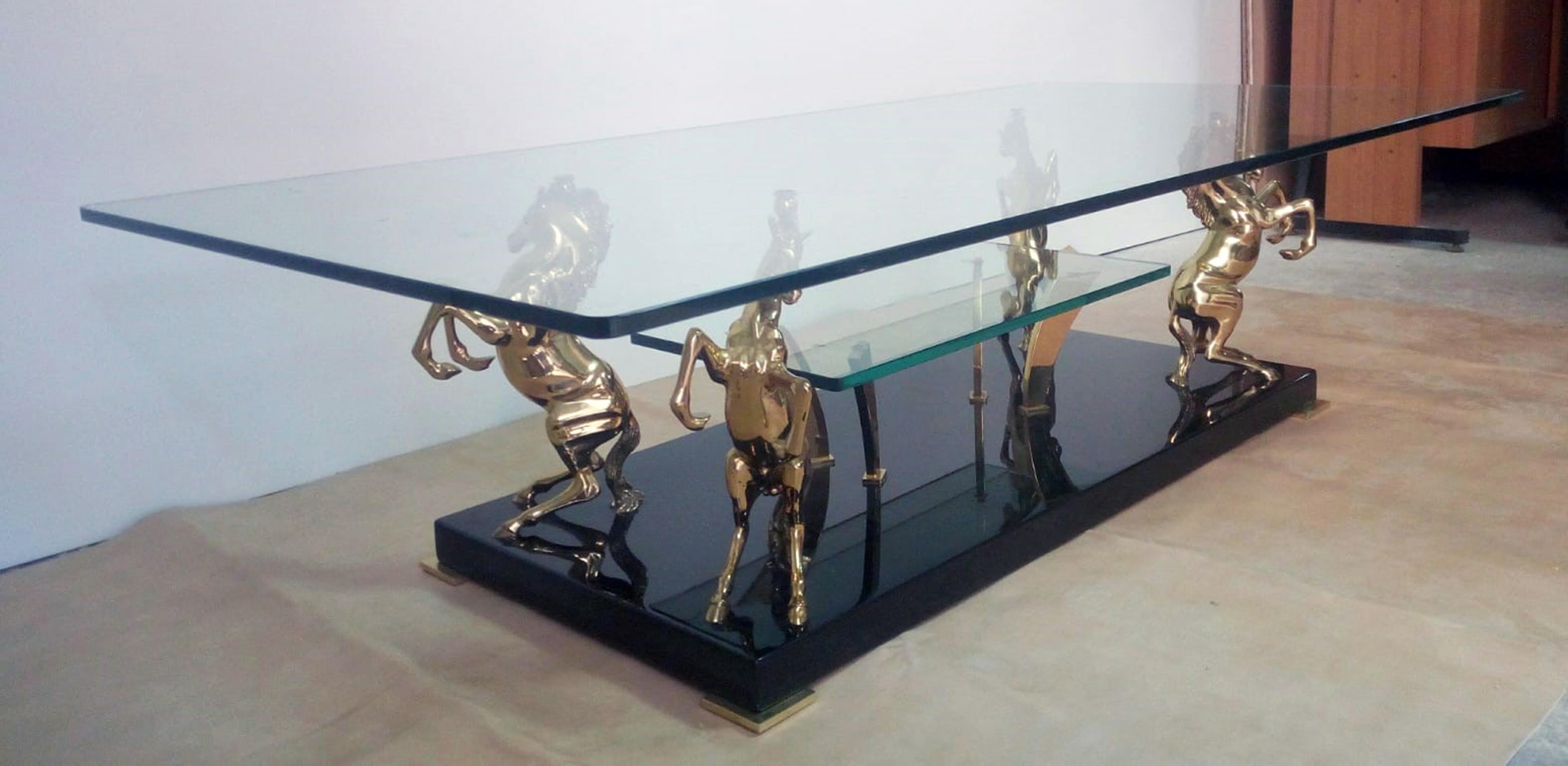 This French coffee table is produced in the 1970s by the Maison Charles. The table has a two-level brass structure, below a smaller crystal and a larger crystal top with grinding. The four polished brass horses rest on a polished ebonized wooden
