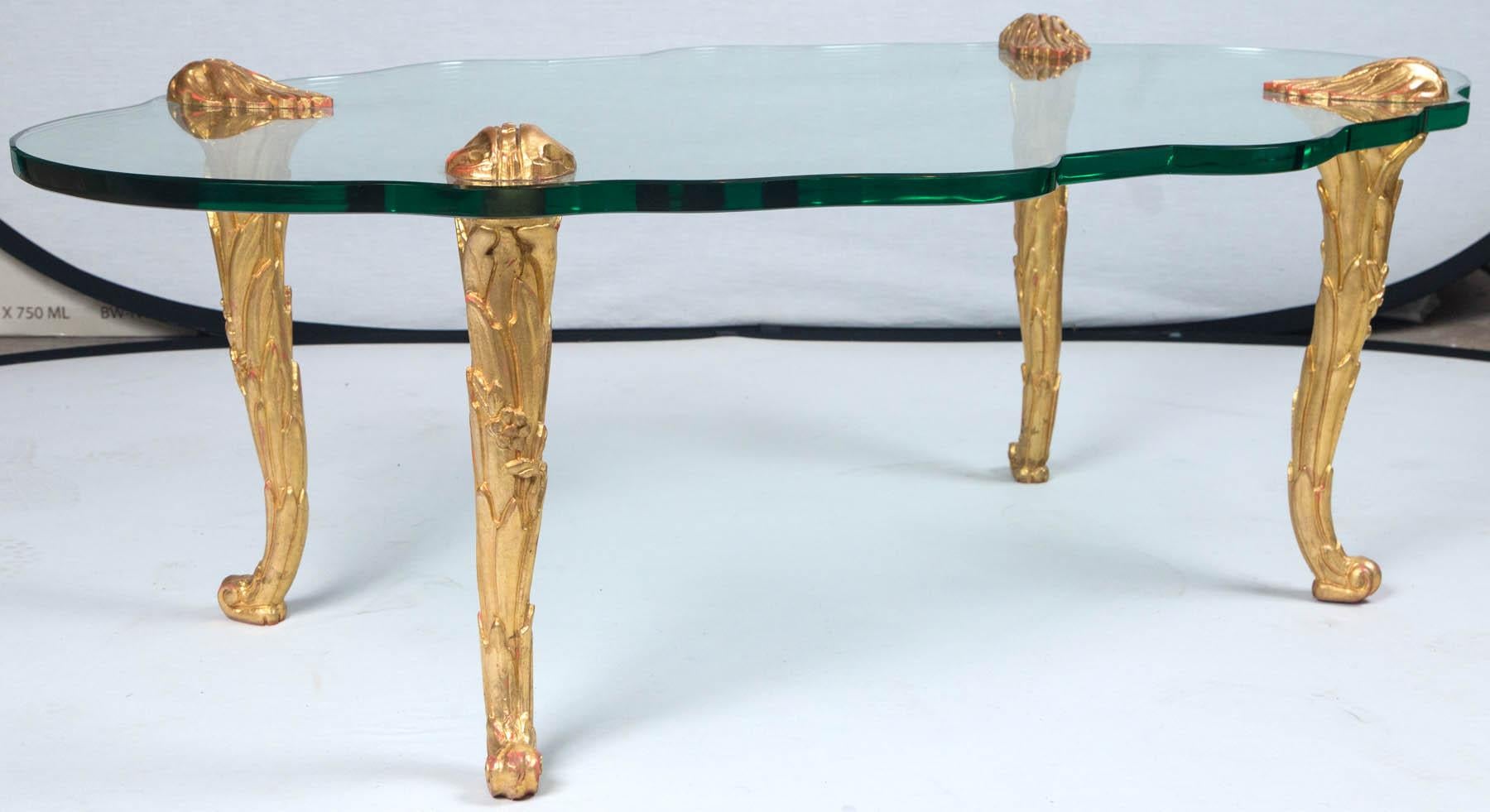 Table basse en verre et bois doré de style Maison Charles, France, vers les années 1960. Plateau en verre épais et incurvé avec pieds encastrés. Merveilleuse surface sculptée et dorée sur les pieds.