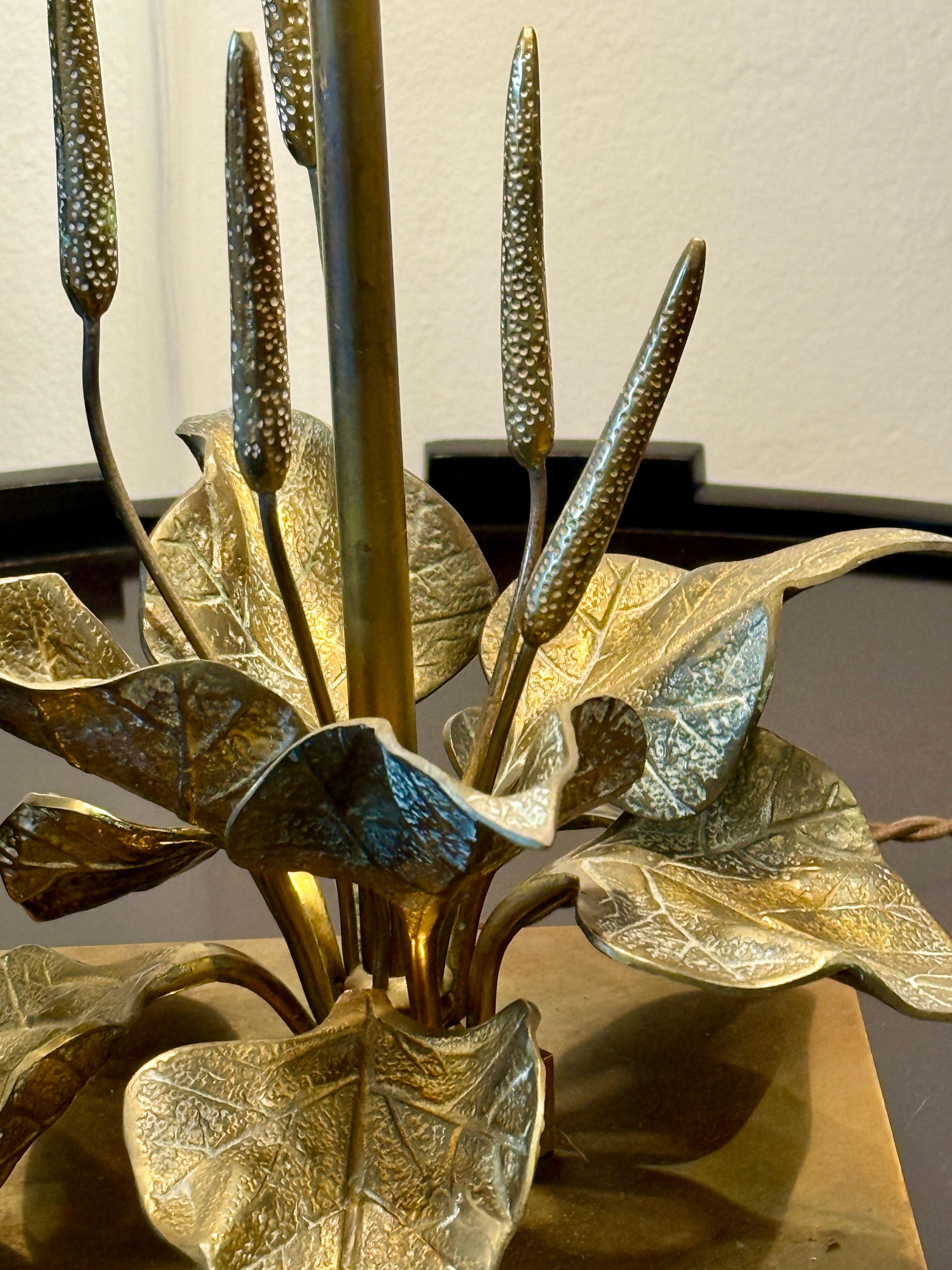 Compuesta por una base cuadrada de latón dorado sobre la que descansan dos hileras de follaje distribuidas por el perímetro de la lámpara y adornadas con finos tallos estilizados de flores de altramuz, todo en bronce dorado.  Una varilla alta de