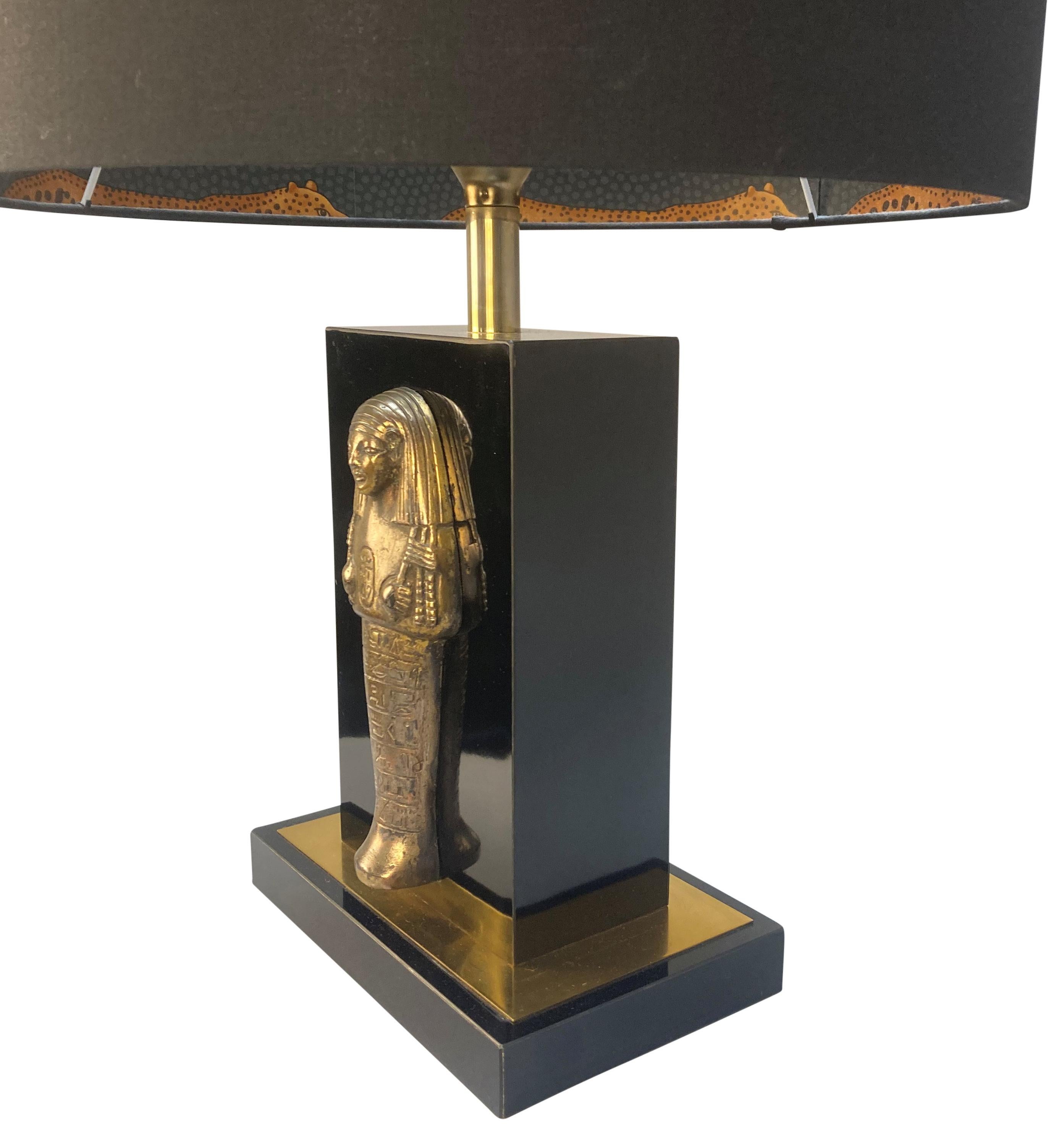 A French table lamp with an Egyptian motif, by Maison Charles. In black resin and brass, with a black drum shade lined with tigers.