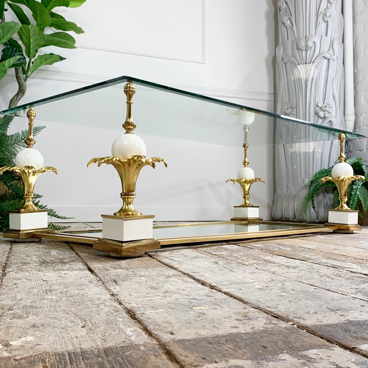 A splendid 1950’s large coffee table by Maison Charles, the bevelled glass top sits upon four carved and lacquered white pineapples, each topped with brass fronds. 

The base is a mirrored plate that sits within the gold table frame. Both the