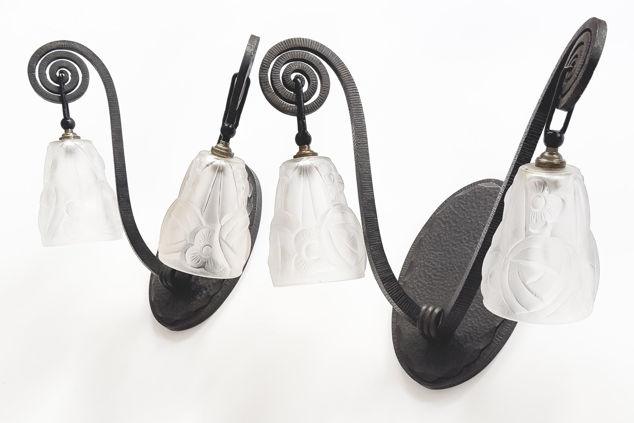 This pair of wrought iron wall lights is a stunning testament to the artistry of Degué, featuring two meticulously molded and pressed smoked glass tulips. Each tulip is elegantly adorned with a delicate decor of stylized flowers and leaves,