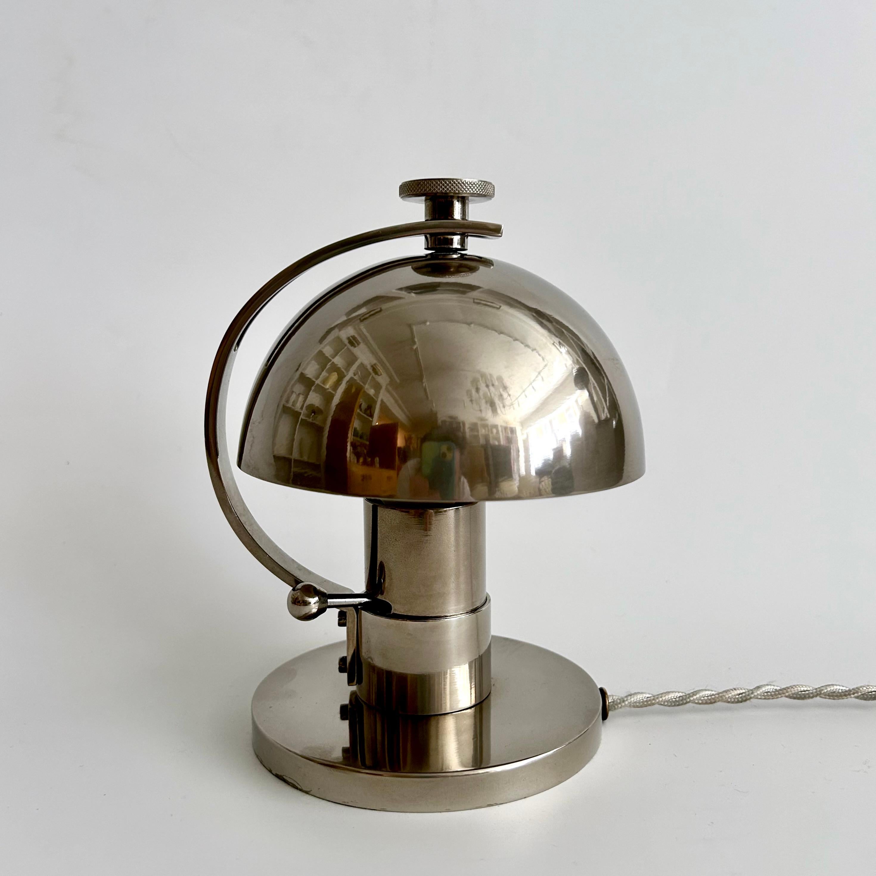 A small nickel-plated bedside lamp by the important French Modernist design studio Maison Desny, circa 1930. 
The lamp has a half-sphere adjustable shade on an arched stem and a cylindrical base. The whole light is adjustable around the base so it