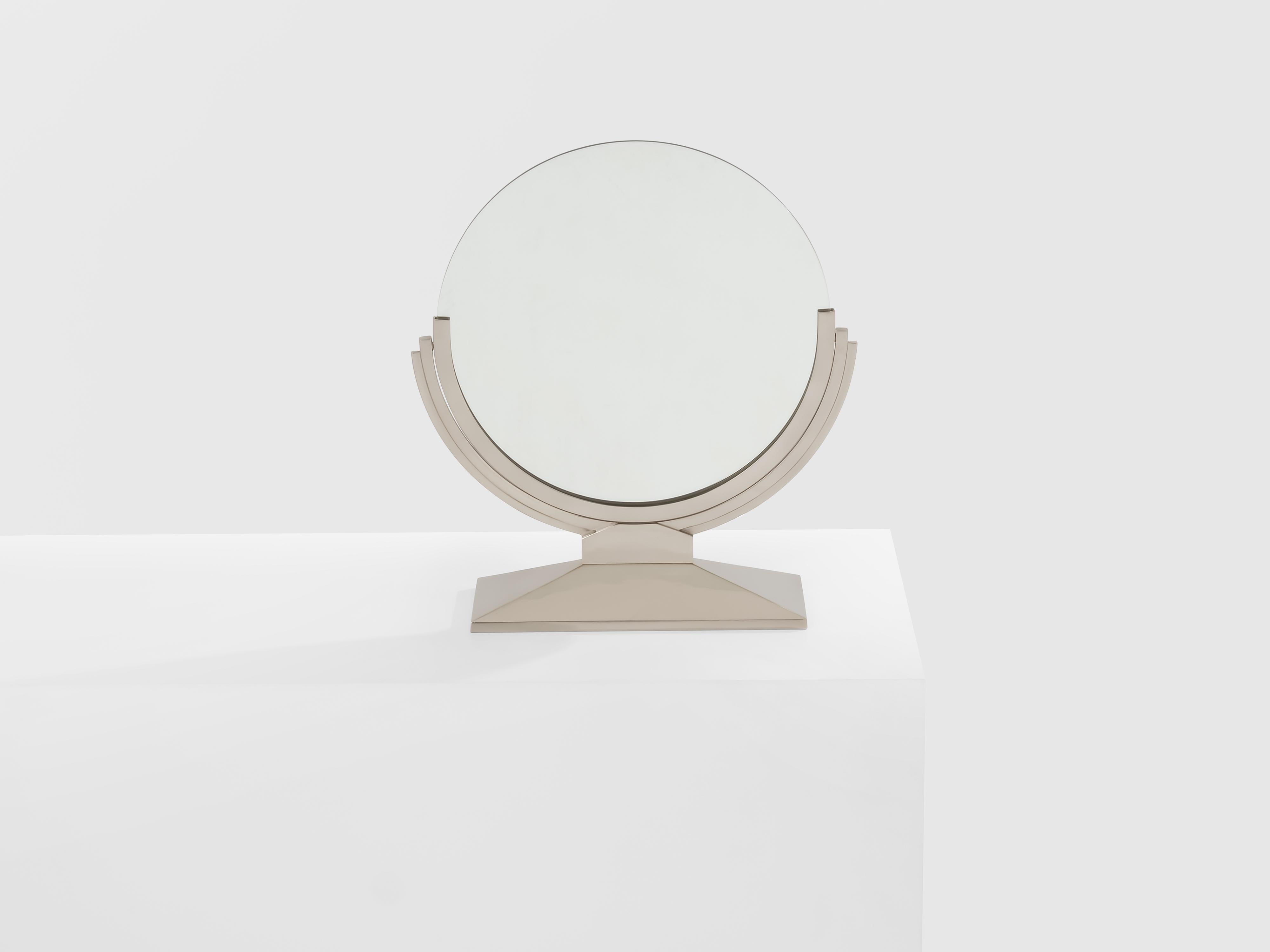 Ce magnifique miroir de table Art déco en métal nickelé a été conçu par André Domin et Marcel Genevrièr pour la Maison Dominique en France dans les années 1930. Il se compose d'une base rectangulaire surélevée et d'un magnifique miroir rond