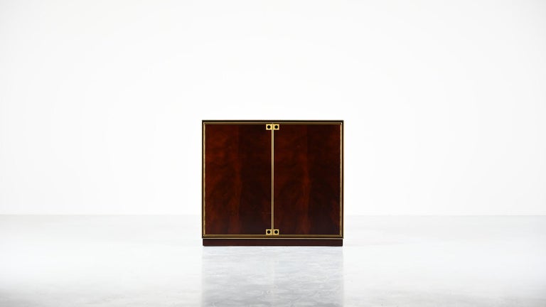 A rare pair of Maison Jansen cabinets. Two doors cabinets made of mahogany and mahogany veneer, enhanced with brass rods and handles. Interior displaying a bronze mirror in the back and adjustable glass shelves. Traces of use such as scratches and
