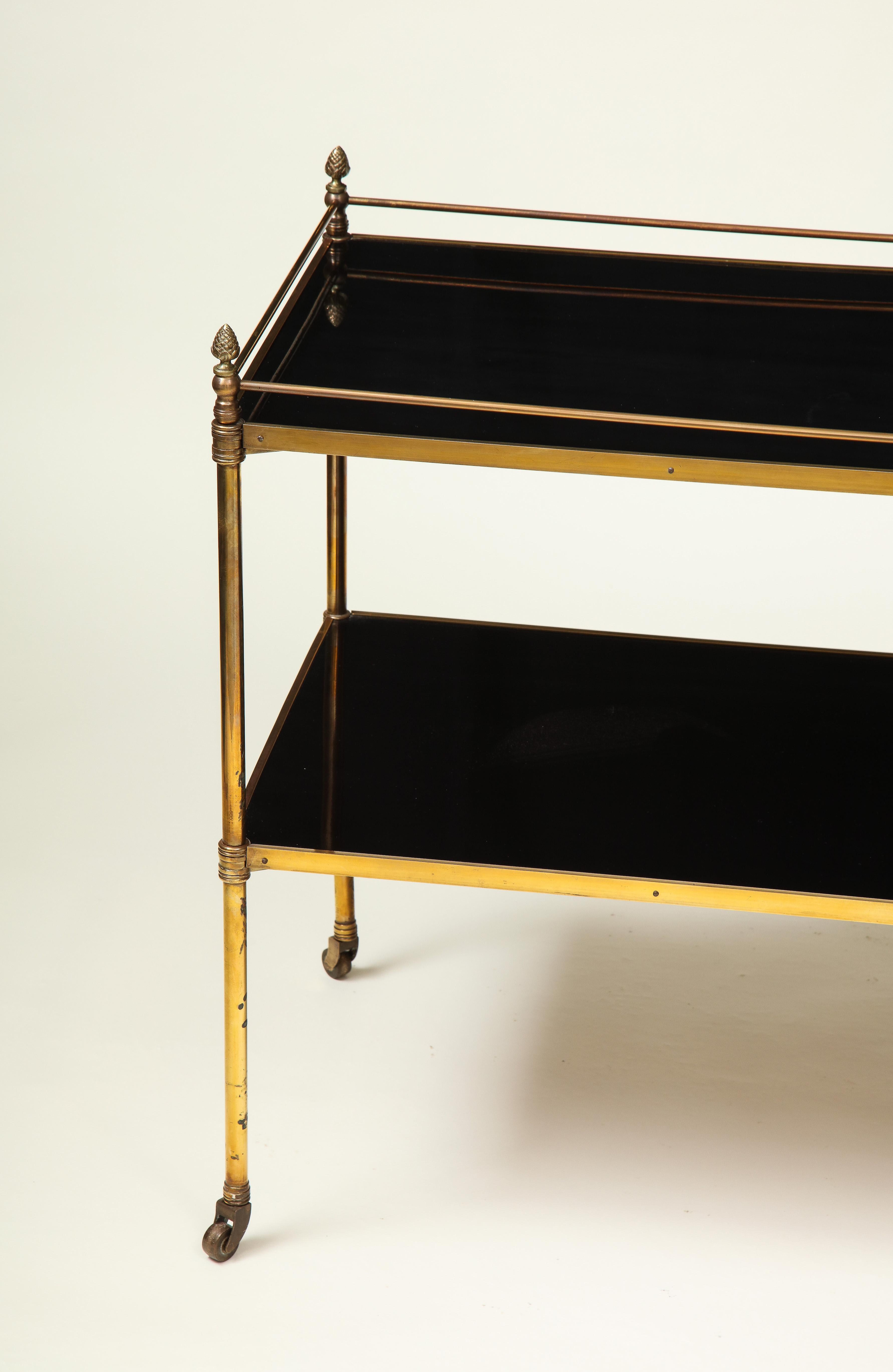 With two long rectangular black glass brass-bound shelves raised on turned uprights surmounted by pine cone finials; on brass casters.

Provenance: From the Collection of Mario Buatta, New York, NY.