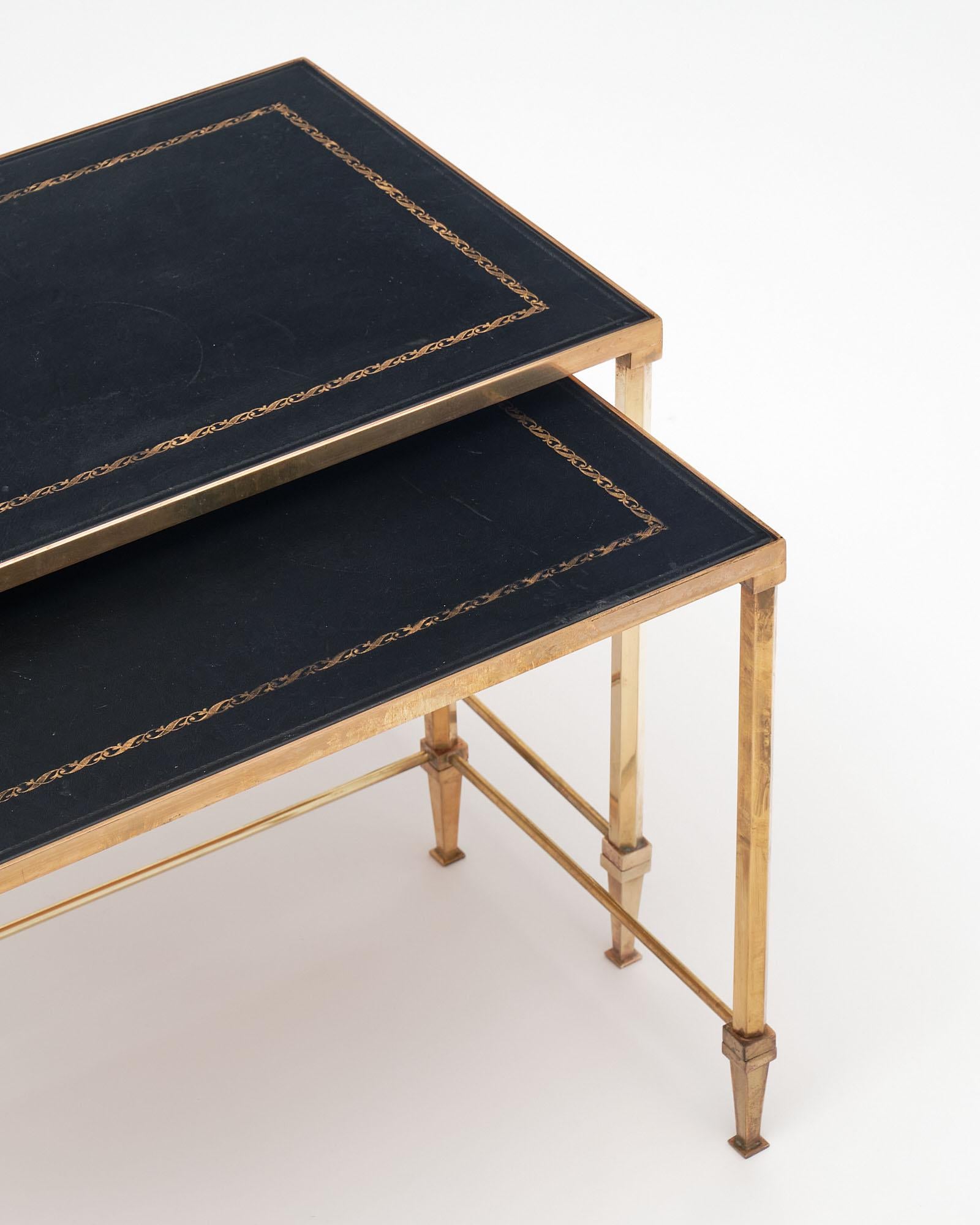 Pair of nesting tables by Maison Jansen. The tops are made of leather with gold detailing supported on gilt brass tapered feet. Dimensions for the smaller table are listed below. 
Measures: L18.5 / D12 / H15.