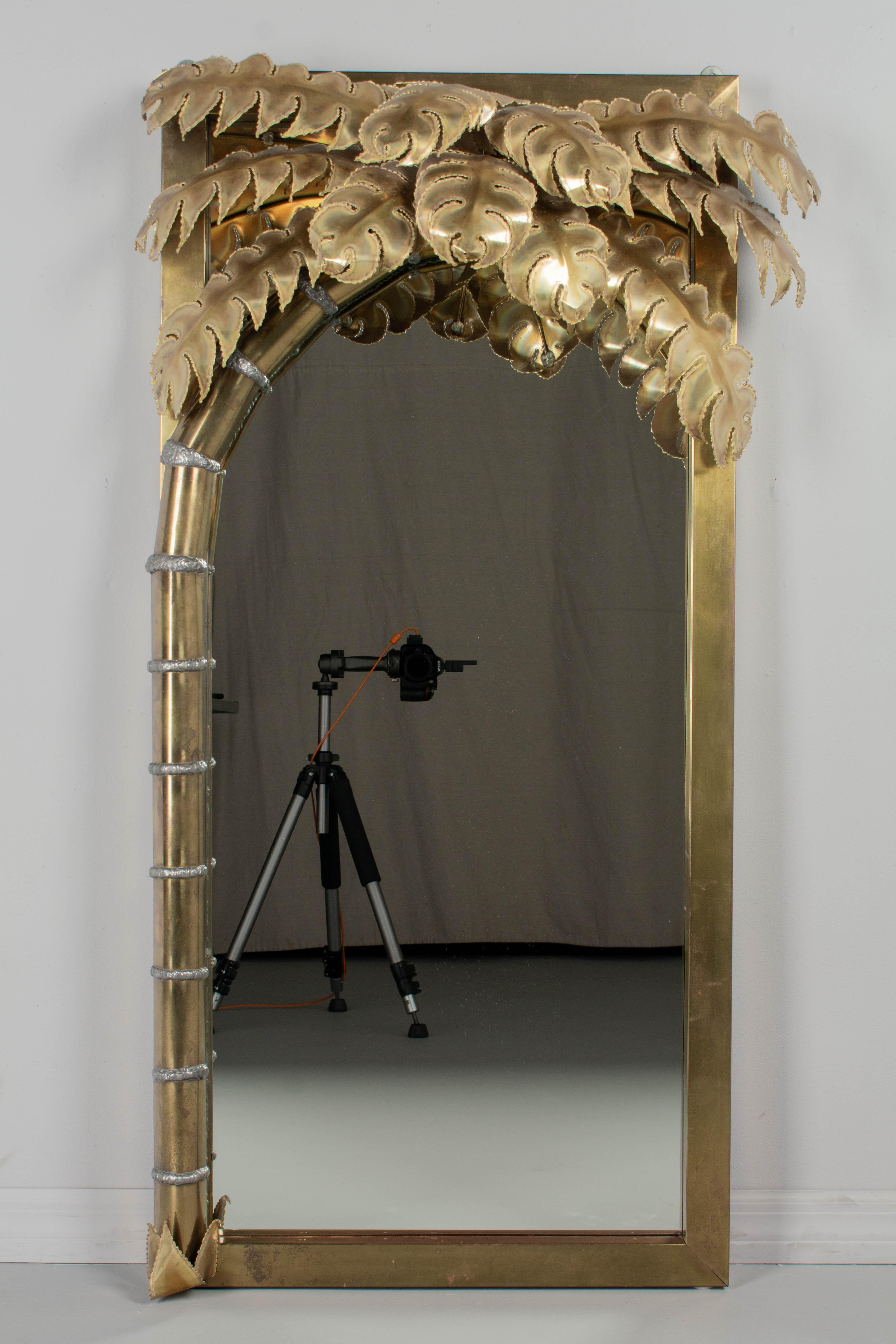 An iconic brass palm tree illuminated wall mirror designed by Christian Techoueyres for Maison Jansen. Crafted of brass sheet metal over wood with a canopy of torch cut and welded burnished brass palm fronds. The metal is in good condition, with a
