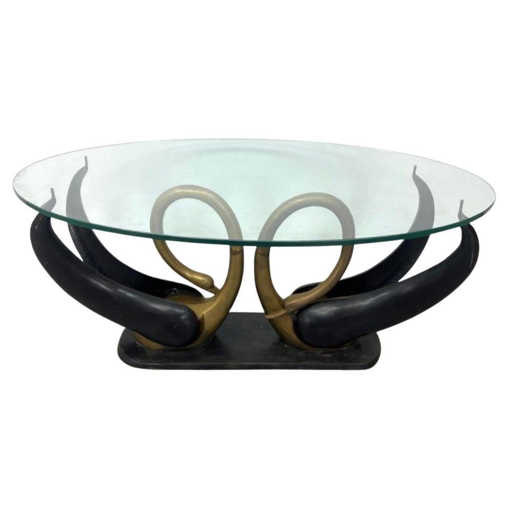 Table basse élégante avec une double base en forme de cygne en laiton. Leurs ailes servent de support à la table. La table basse est dotée d'un lourd plateau ovale en verre transparent. Cette table basse/cocktail au design Hollywood Regency attire