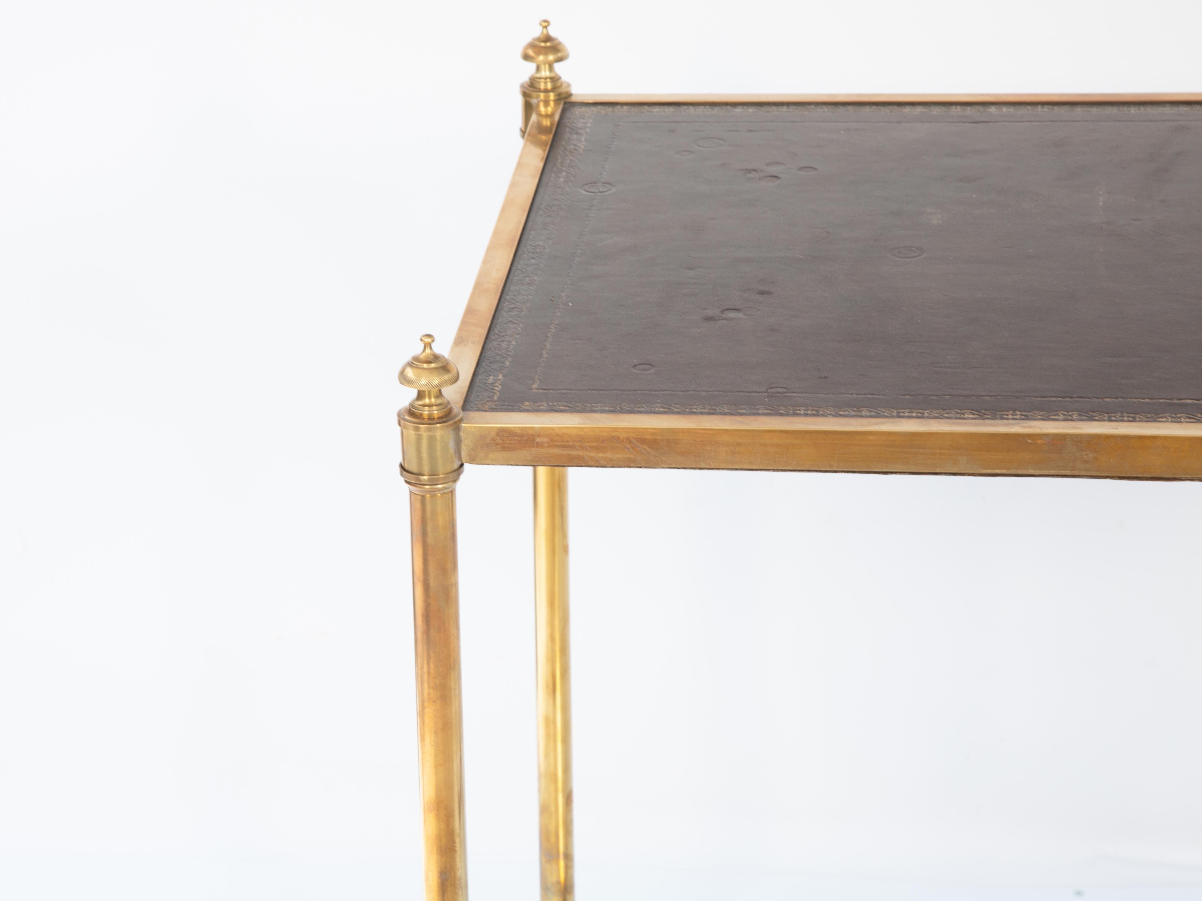 Mesa de té de la Maison Jansen, de latón, con tablero rectangular de piel labrada, elevado sobre patas redondas con remate, unidas por un estante de cristal, que terminan en afiladas patas de clavija. 

Altura de la mesa: 27,75

Ponte en contacto