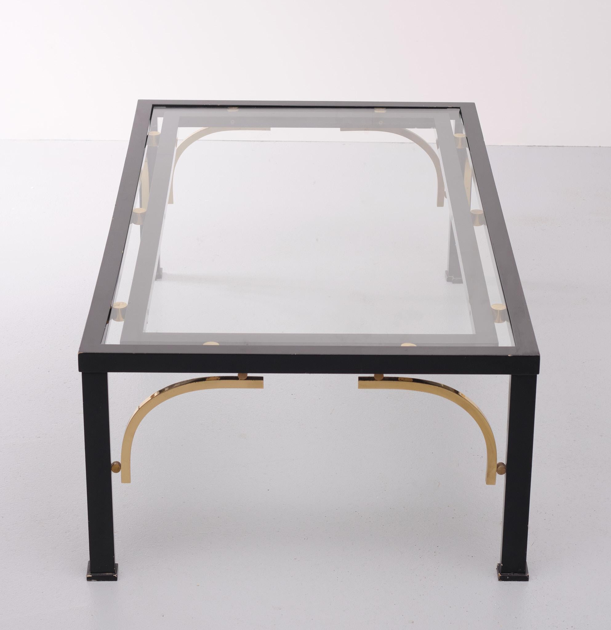 Unique coffee table. Made with wooden feet black metal base and brass 
details. New glass top. Attributed to Maison Jansen 1970s Very stylish table.