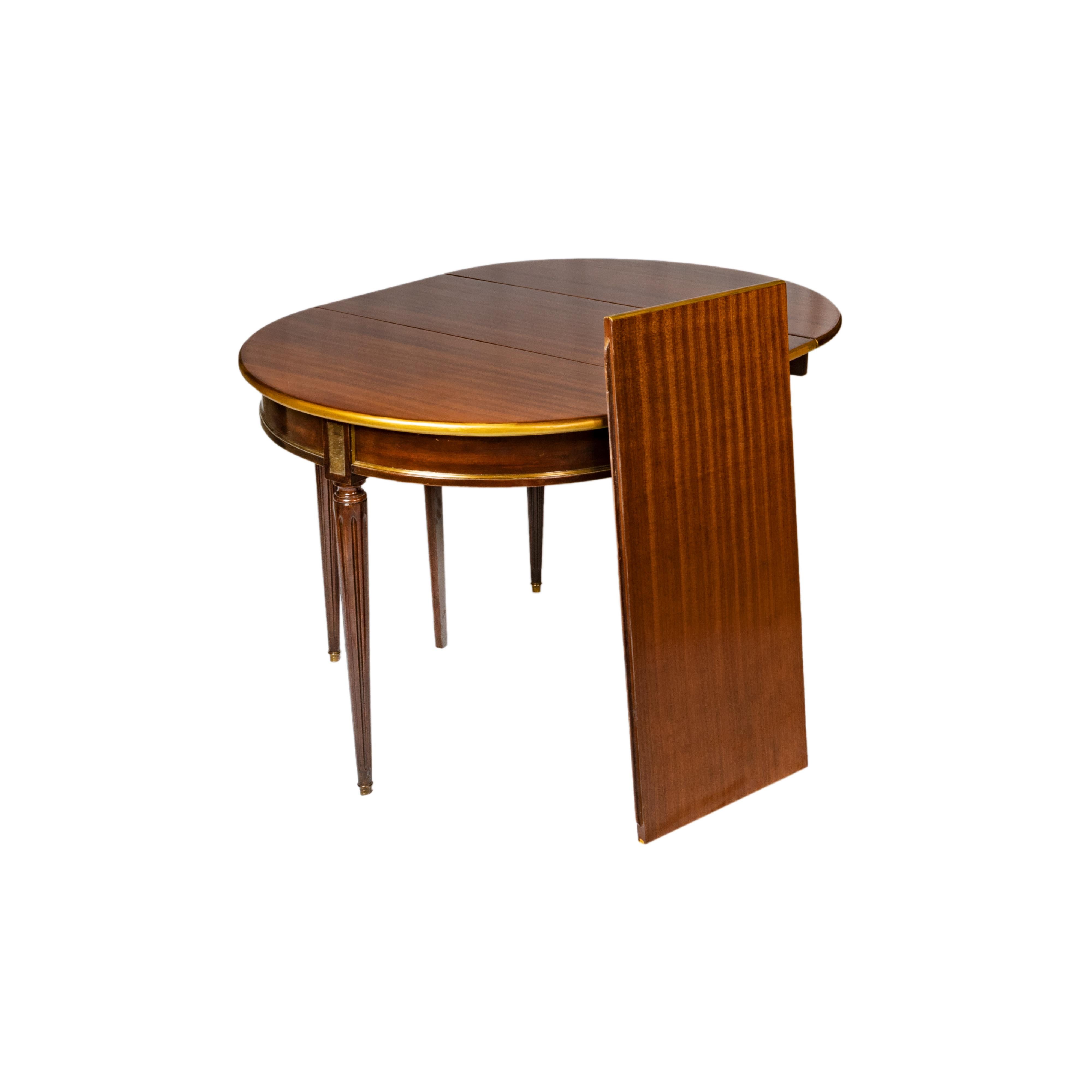 Une table de salle à manger raffinée de style Directoire de la Maison Jansen avec des montures en laiton, inspirée par l'esthétique de Hepplewhite. Cette élégante table de salle à manger présente un design polyvalent avec deux rallonges et des pieds
