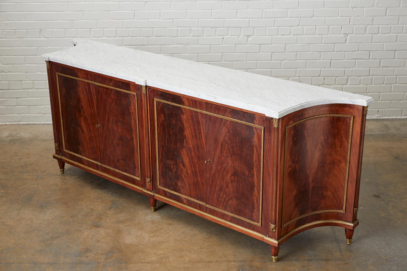 Grand Directoire style mahogany and marble sideboard server in the style of Maison Jansen. This monumental sideboard features radiant crotch mahogany that is showcased on the front and sides. Embellished with bronze framing and mounts in the French
