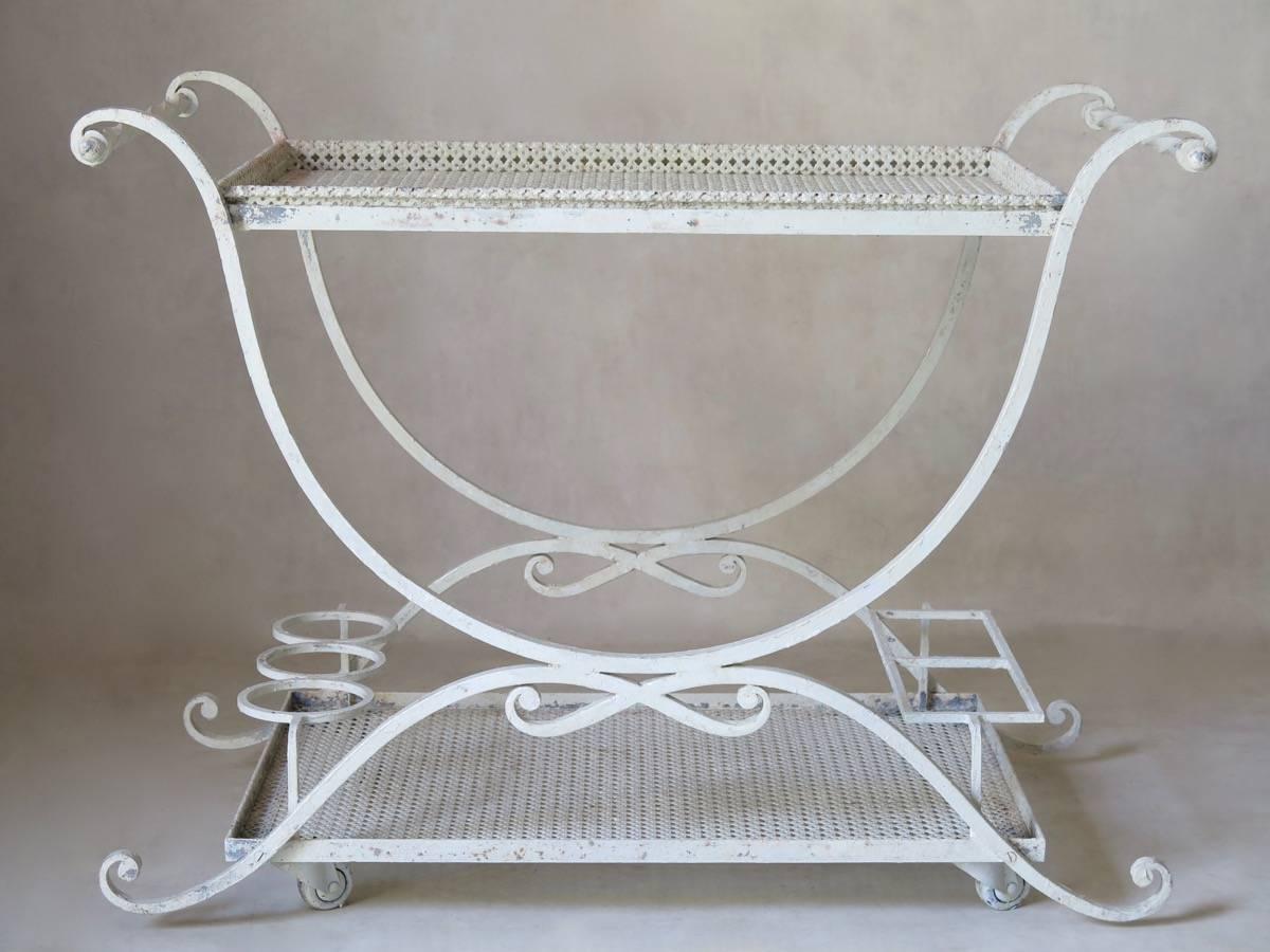 Charming wrought iron bar cart or trolley with two trays (the top one removable) in cloverleaf patterned sheet metal. Elegant and refined details: Curule-shape base, scrolling outwards at top and bottom; bow detail, twisted iron handles.
 