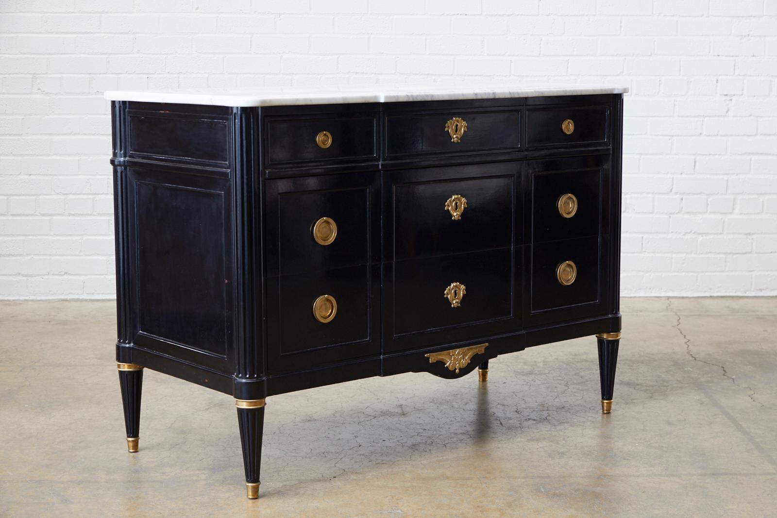 Dramatic ebonized commode or chest of drawers featuring an escritoire or secretaire drop down writing table. Made by Maison Jansen in the Louis XVI style with a carrara marble top. Beautifully crafted with reeded pillar style column corners. The