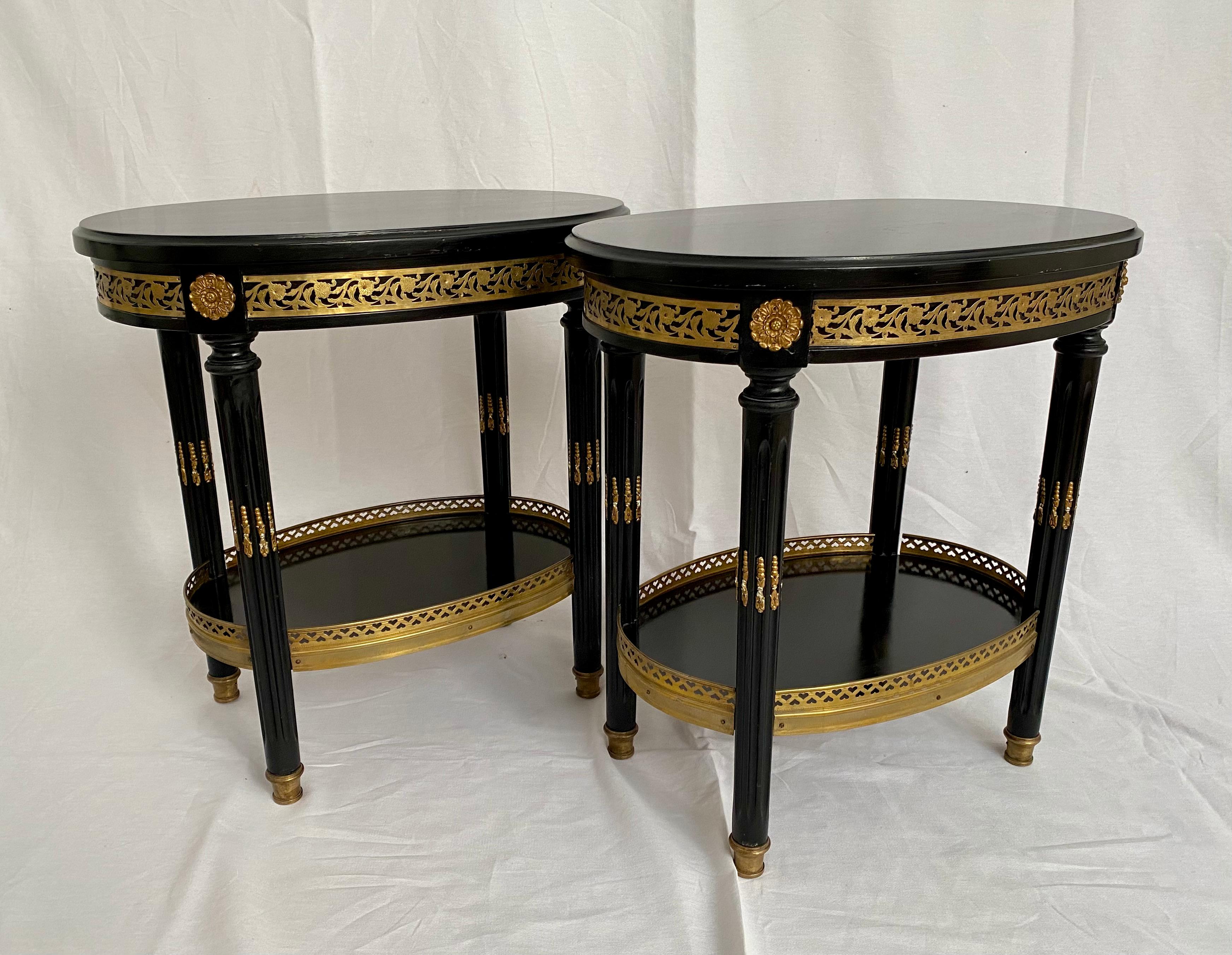 Rare, stamped, Maison Jansen, pair of French Louis XVI style ebonized oval side tables, in the glamorous style of Hollywood Regency. This two-tiered, pair of black lacquer tables is composed of ebonized wood with tôle and bronze hardware detail,