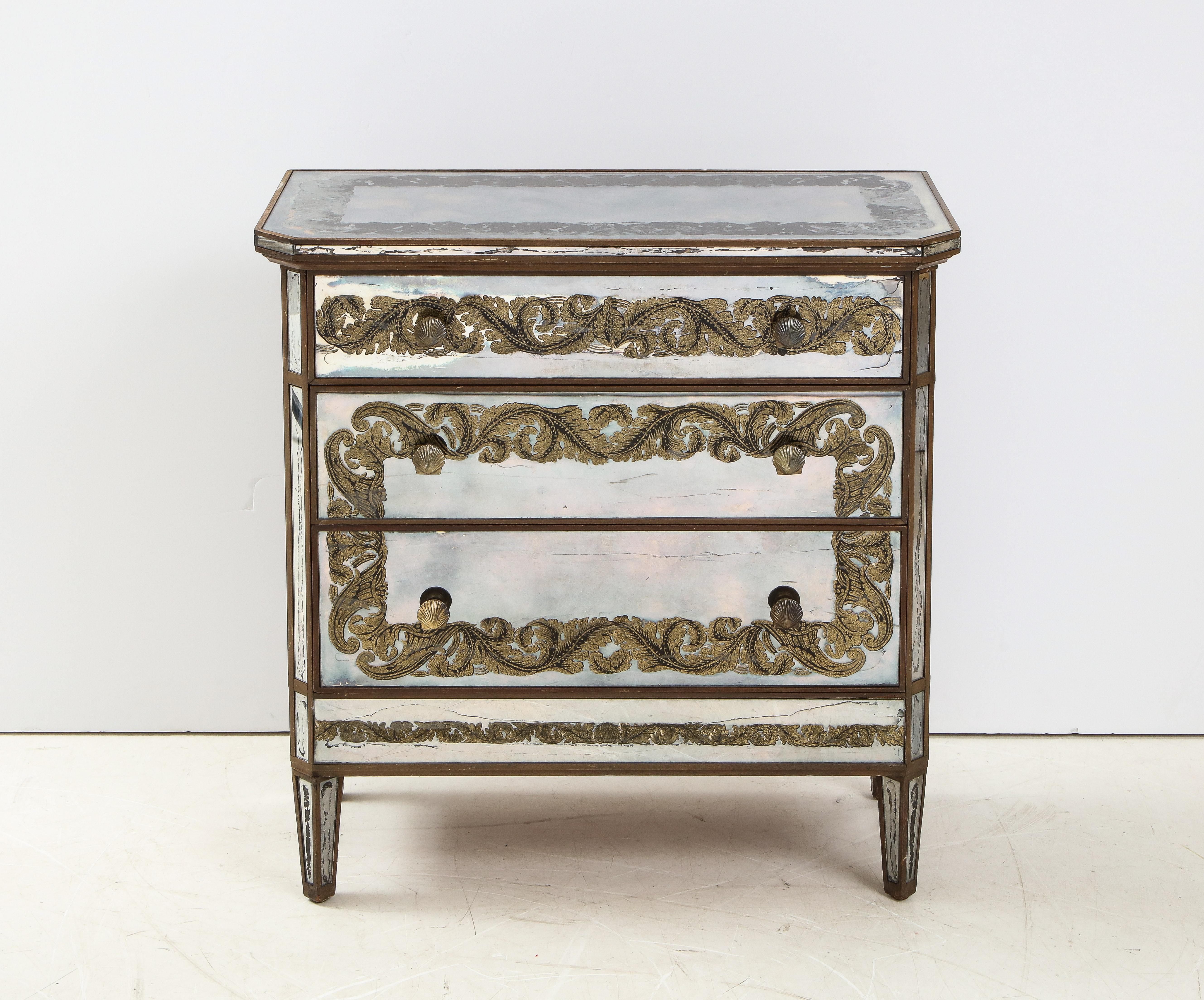 An elegant Maison Jansen eglomisé three draw chest with gold gilded decoration of cornucopia shells with floral bouquets and scrolls of acanthus leaves on mirrored panels. A gilded trim surrounds the mirrored panels and two shell form pulls are on