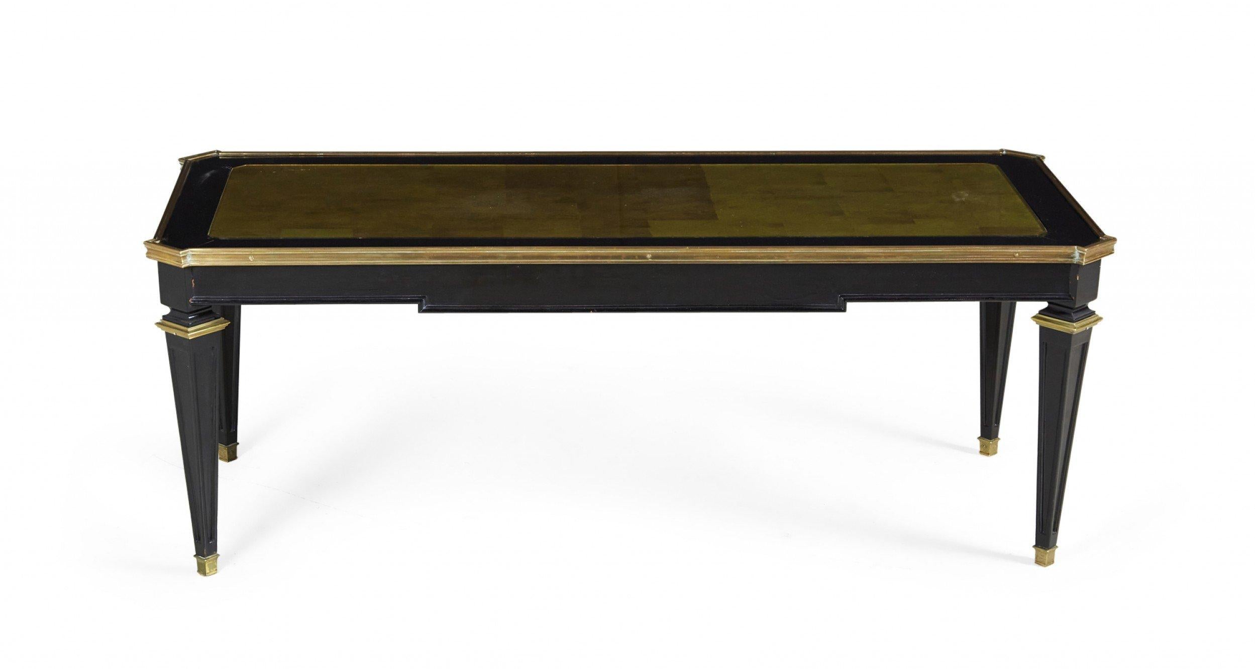 French mid-century (1940s) ebonized wooden coffee table with gilt painted trim, an inset gold glass top with geometric pattern, and four tapered square legs ending in brass sabots. (Maison Jansen).
  