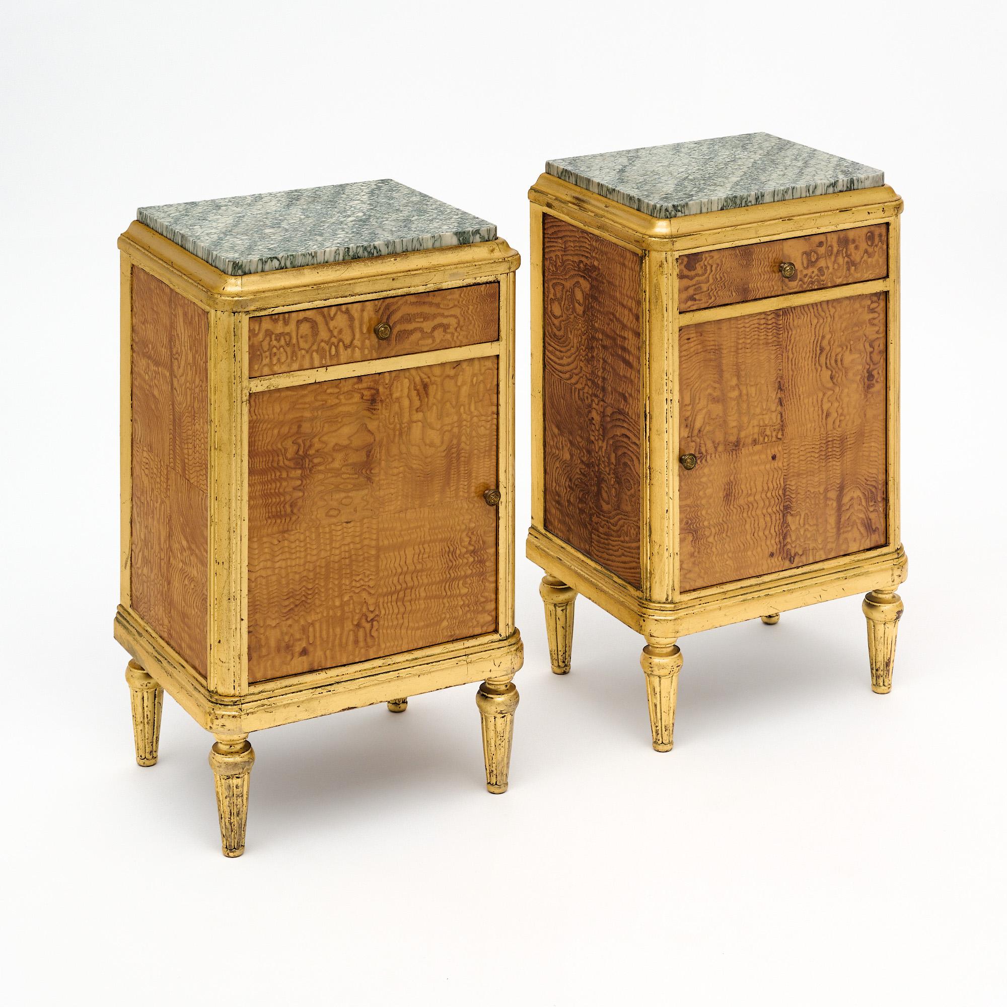 Bed Side tables from the period in France. The body of the cabinets is crafted with burled elm wood on the front of the doors, dovetailed drawer, and sides. Each features the original knobs. The legs and trim throughout are gold leafed. The doors