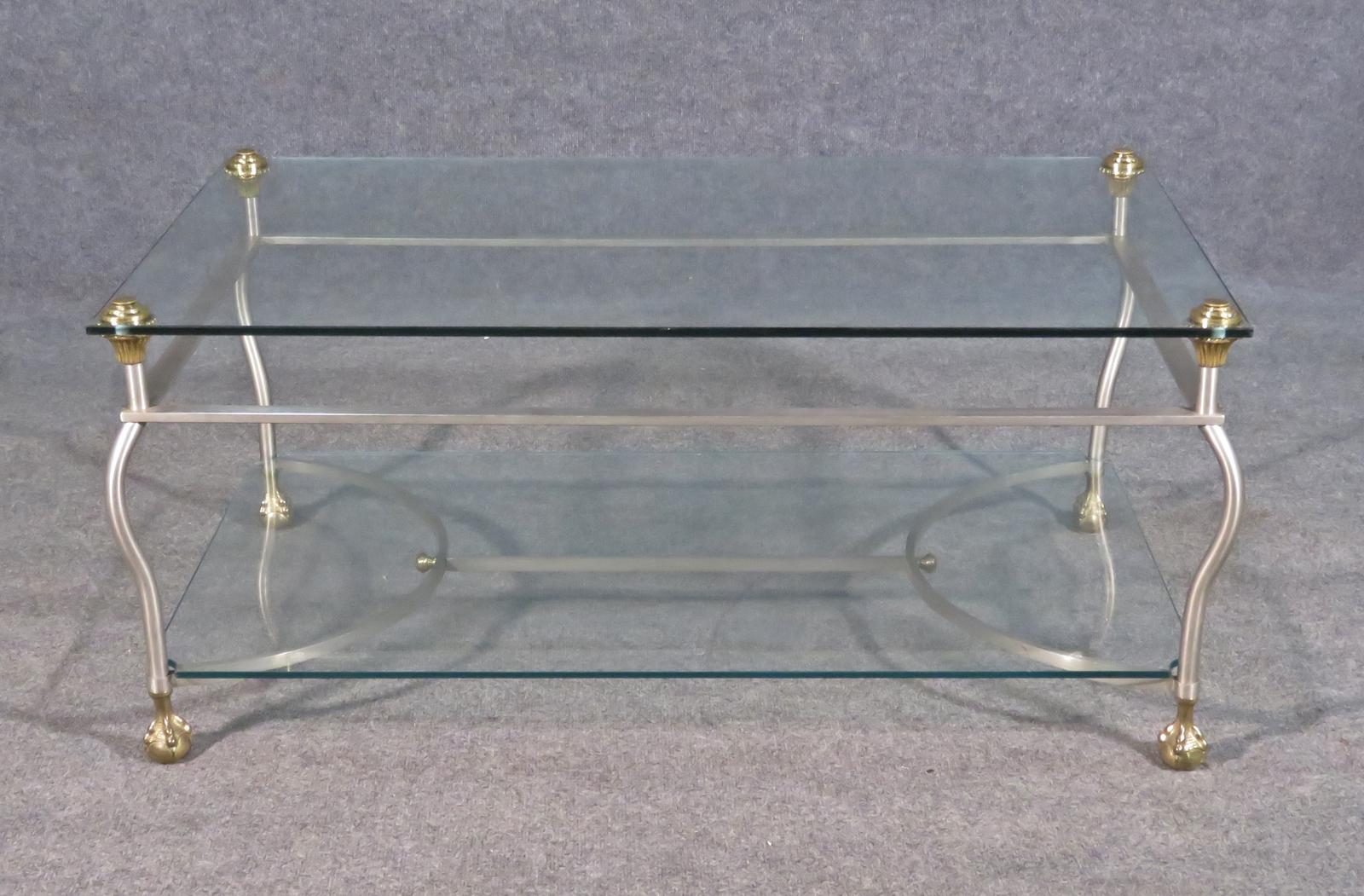 This is a gorgeous Maison Jansen coffee table with steel, glass and brass trim. The table is in good original condition and ready to take home. Chrome frame. Brass accent. Ball and claw feet. 2 tier. Glass shelves. Measures: 18 3/4