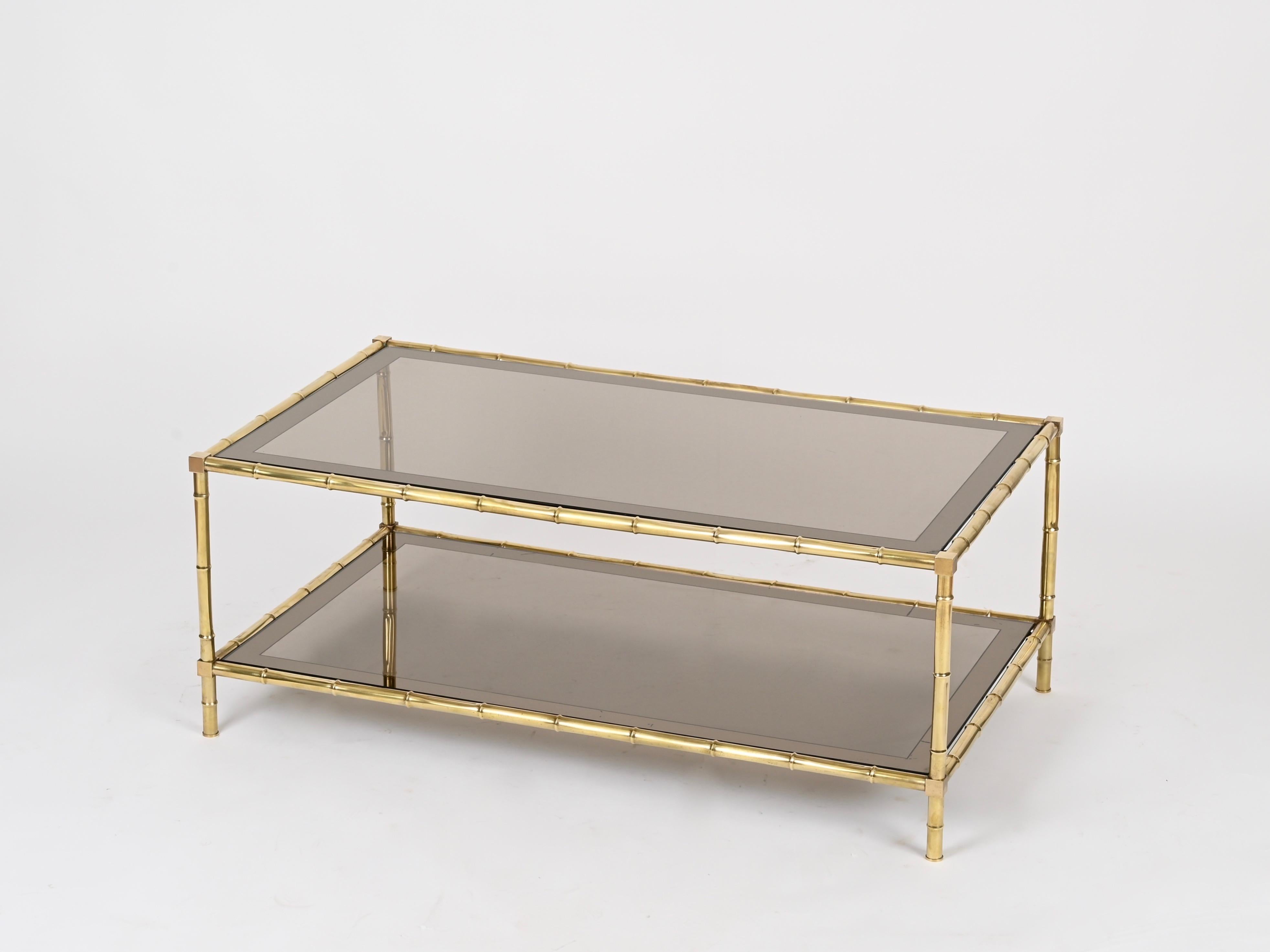Maravillosa mesa de centro grande de latón con efecto bambú completada con dos tableros de cristal ahumado con borde de espejo. Esta pieza increíblemente elegante y única fue fabricada por la Maison Jansen en Francia durante la década de
