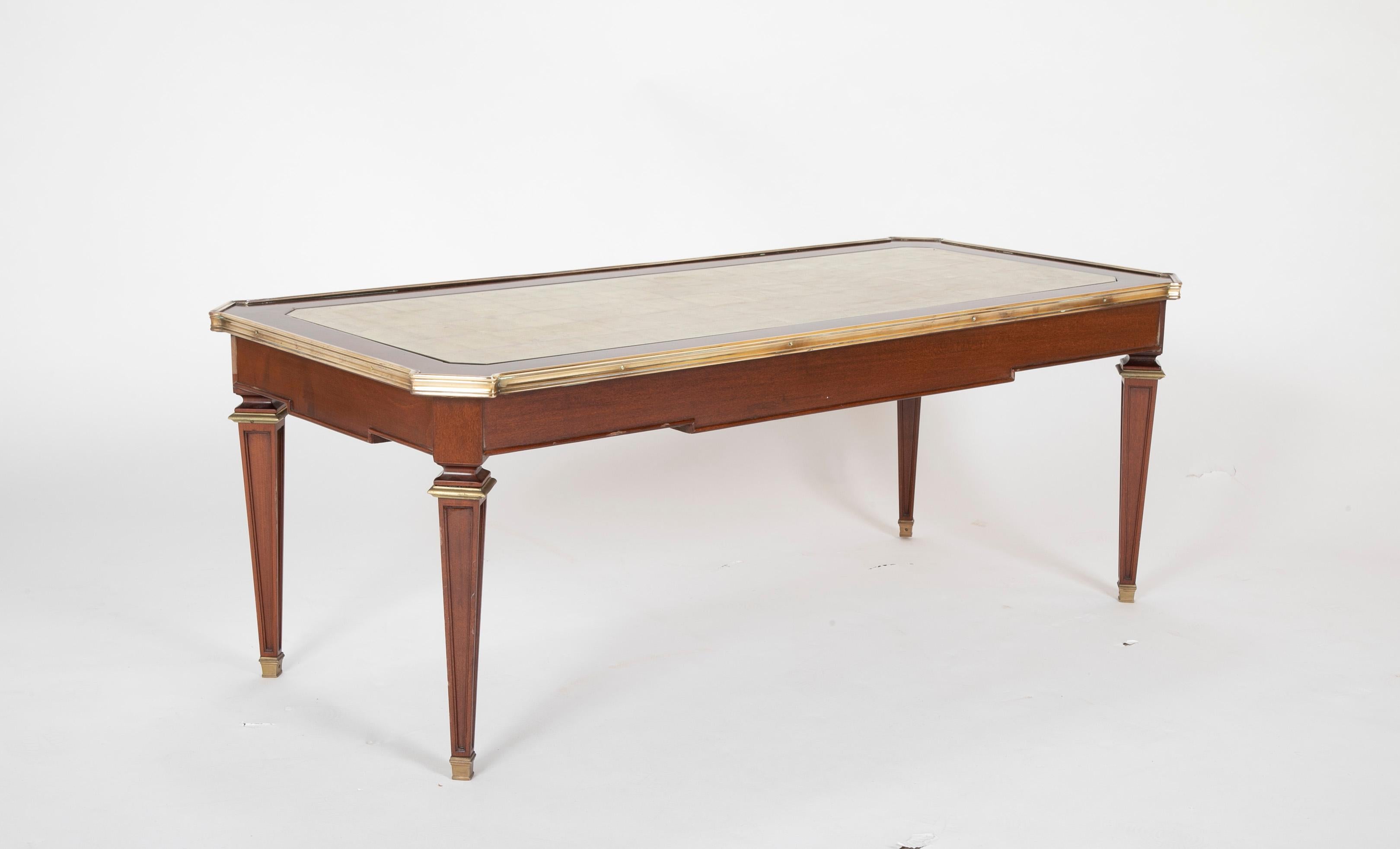 A graceful and stylish French mahogany coffee or cocktail table with bronze mounts and feet and an exquisite gold leafed glass inset top. A modern, elegant midcentury interpretation of the Louis XVI style by Maison Jansen, Paris.

Provenance: