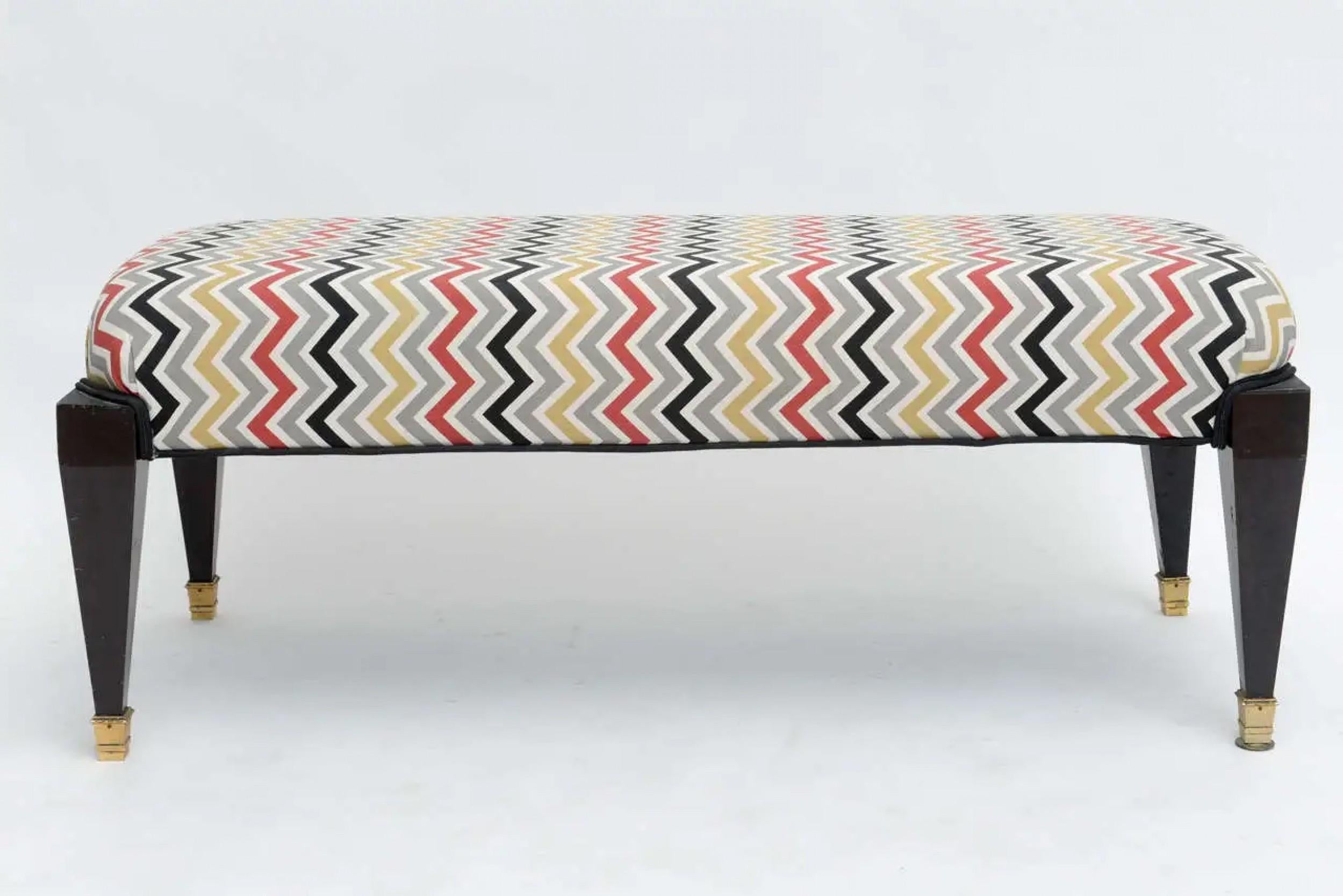 Midcentury (1940s) French Neo-classic Style ebonized rectangular bench with padded seat upholstered in a multicolor zigzag pattern, resting on 4-sided tapered legs ending in brass sabots. (attributed to MAISON JANSEN).