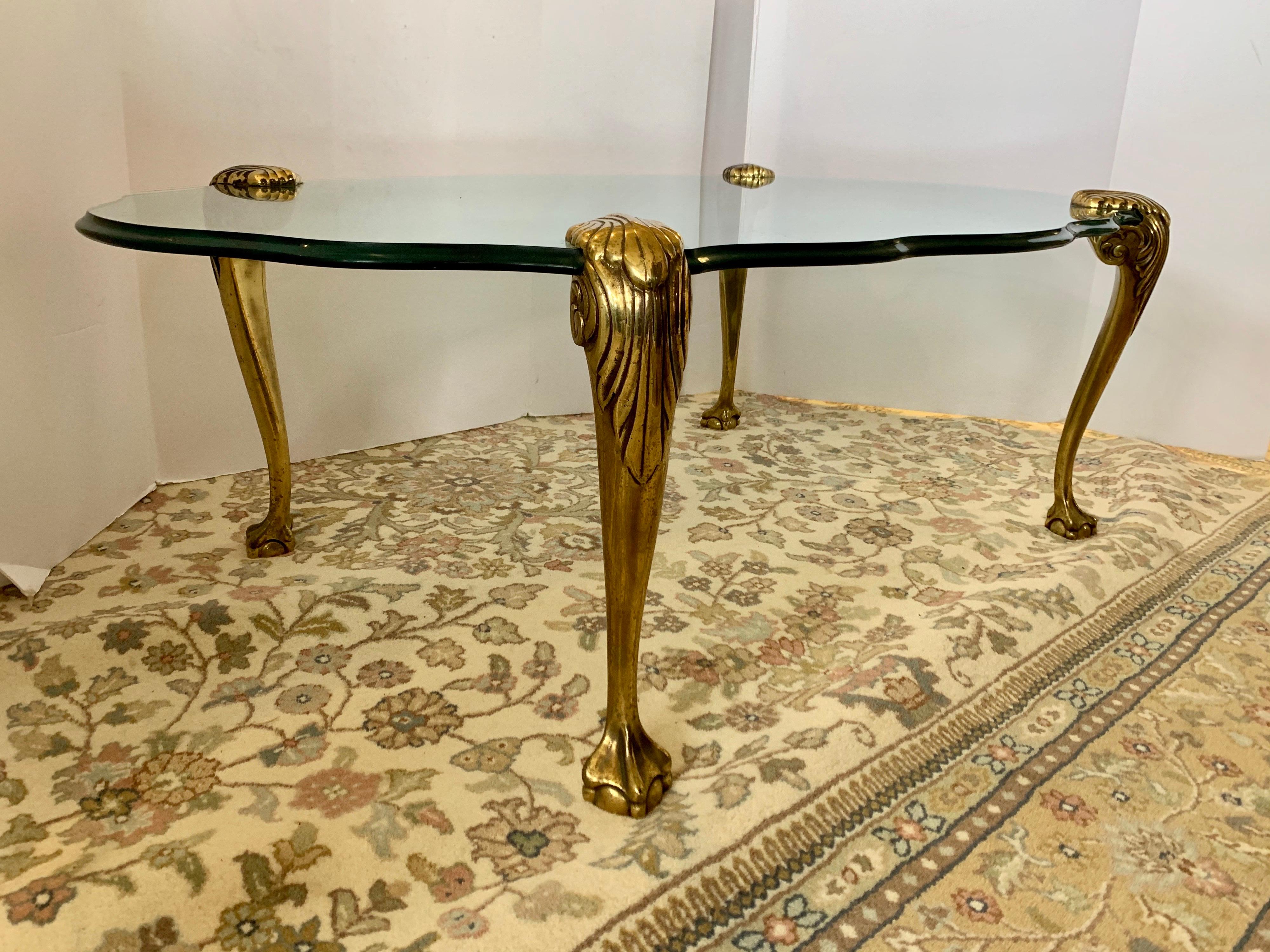 Elegant 1960s Maison Jansen midcentury cocktail table with fitted heavy brass legs that slide
in and out. The rare and coveted cocktail table has very thick beveled glass and a magnificent
serpentine like shape. Each of the ornate brass legs