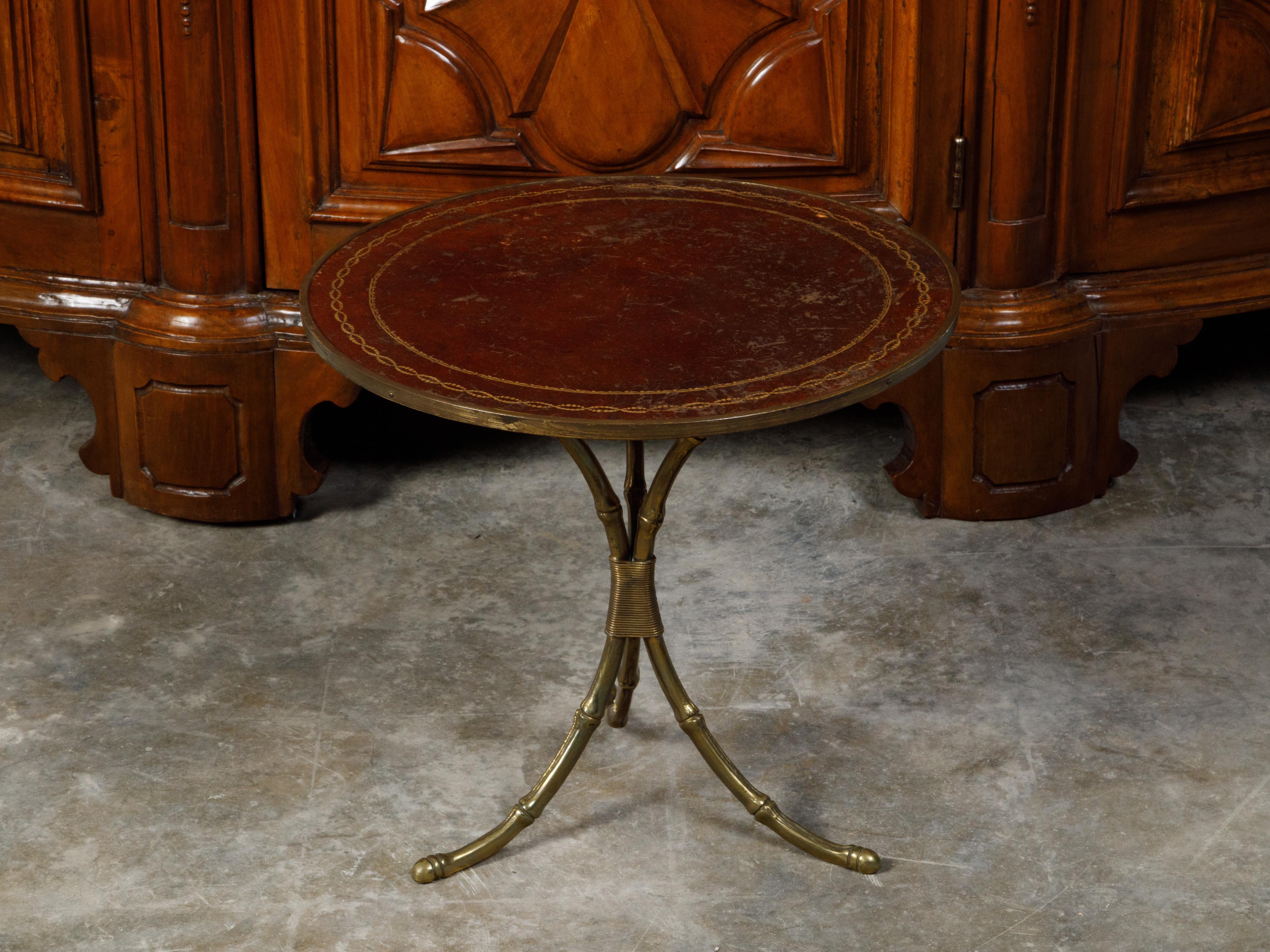 A French Maison Jansen brass side table from the mid 20th century, with leather top. Created in France during the Midcentury period, this Maison Jansen table features a circular brown leather top with gilt motifs, sitting above a faux bamboo brass