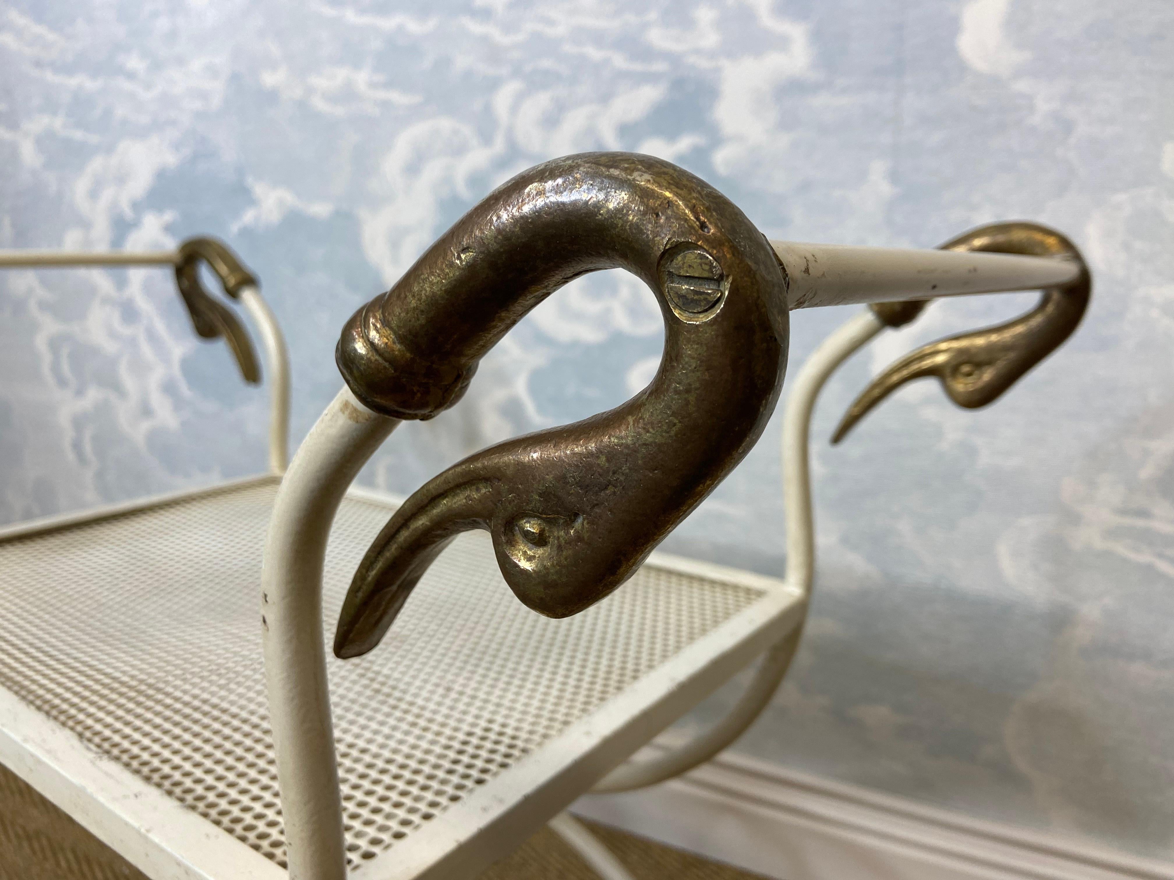 This Maison Jansen style, swan necked curule seat in neo-classical design would make for a charming side table in the pool area or, as intended, as a seat in an outdoor setting.

Made from white lacquered metal with beautiful brass details this seat