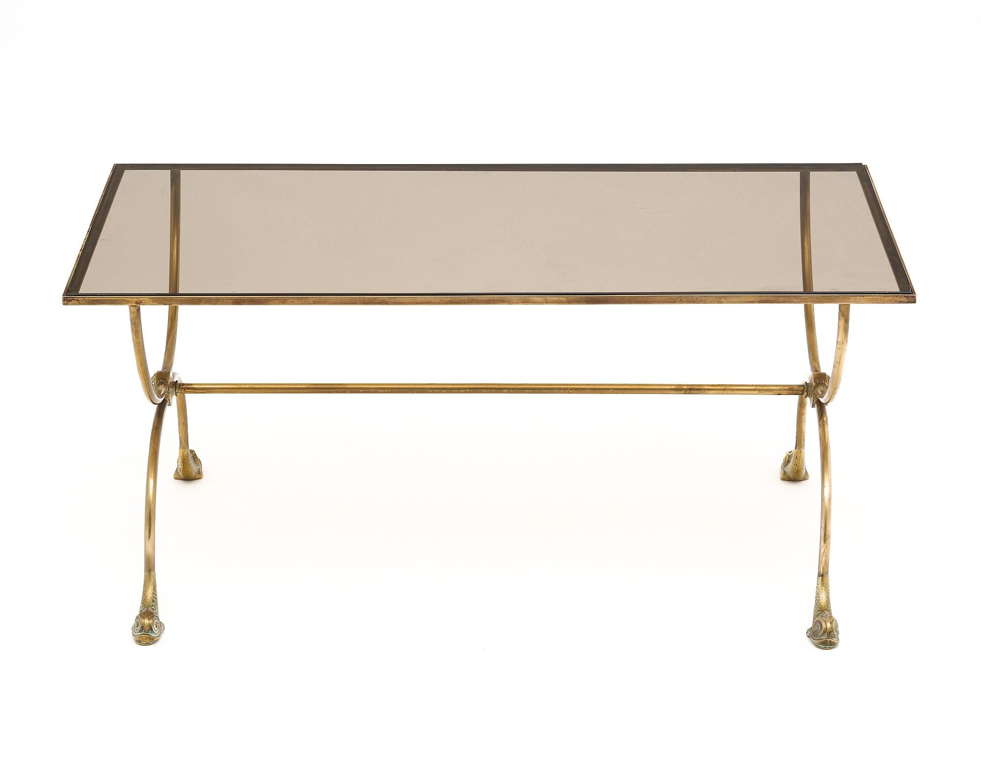 Neoclassical style coffee table made with a brass structure and smoked glass top. This piece by French design house Maison Jansen features curule legs with stretcher and dolphin head feet.
