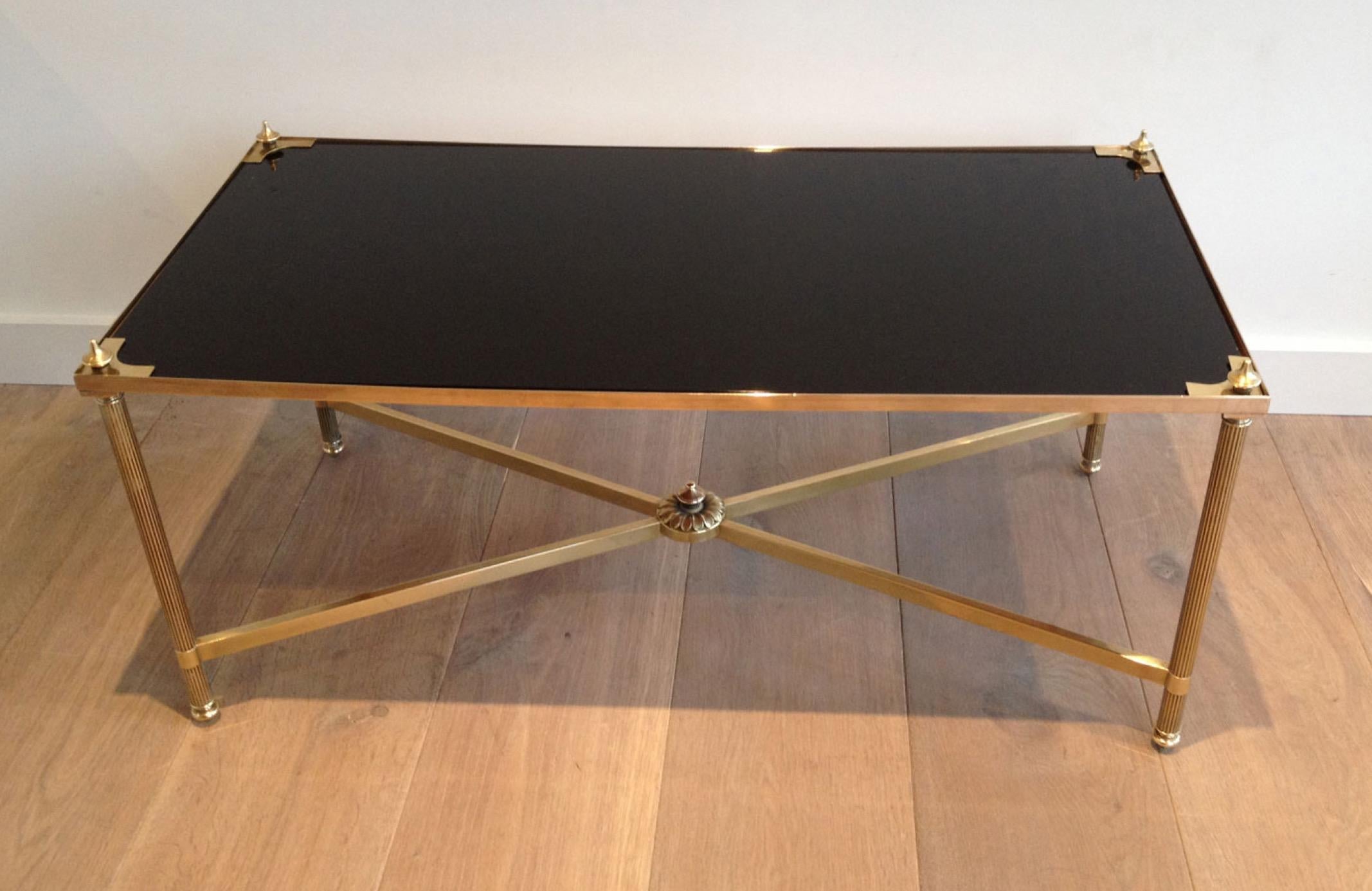 This nice neoclassical style rectangular coffee table is made of brass with fluted legs and a stretcher on the bottom part. It has a black lacquered glass shelf on top with brass triangle and finials on each corner. This is a very elegant cocktail