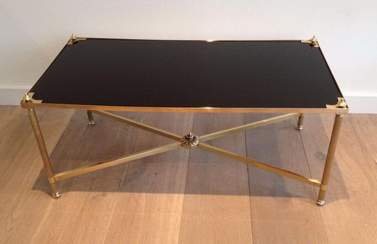 Questo grazioso tavolino rettangolare in stile neoclassico è realizzato in ottone con gambe scanalate e una barella nella parte inferiore. Ha un ripiano in vetro laccato nero sulla parte superiore con triangoli e terminali in ottone su ogni angolo.