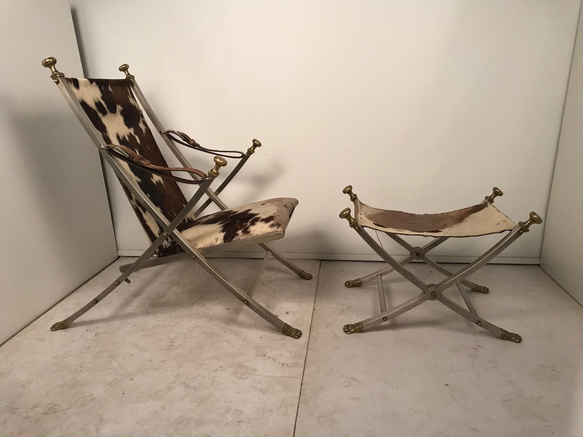 Designed b Otto Parzinger for Maison Jansen, this brushed steel campaign chair pays homage to the ancient world. It is designed like a folding deck chair with a matching stool, both with brass cappings and ornamental finials. The seat and stool