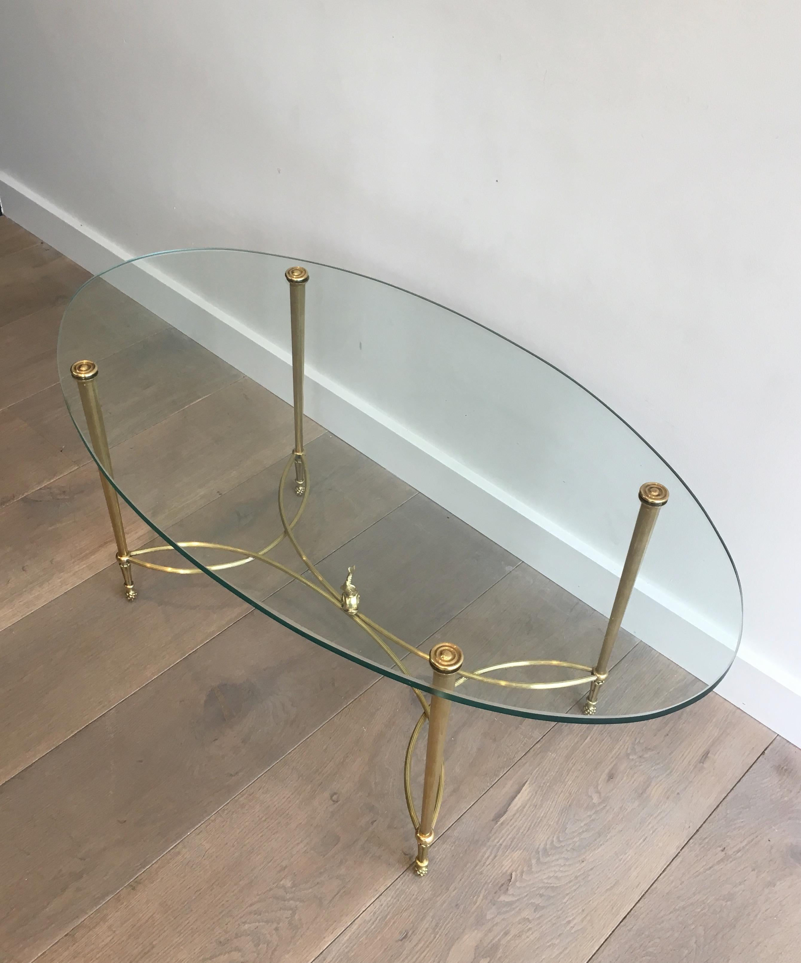 This very nice neoclassical style oval coffee table is made of a brass base with a oval clear glass on top. This cocktail table has a nice stretcher with a dolphin on its center. This is a very fine work by famous French designer Maison Jansen,