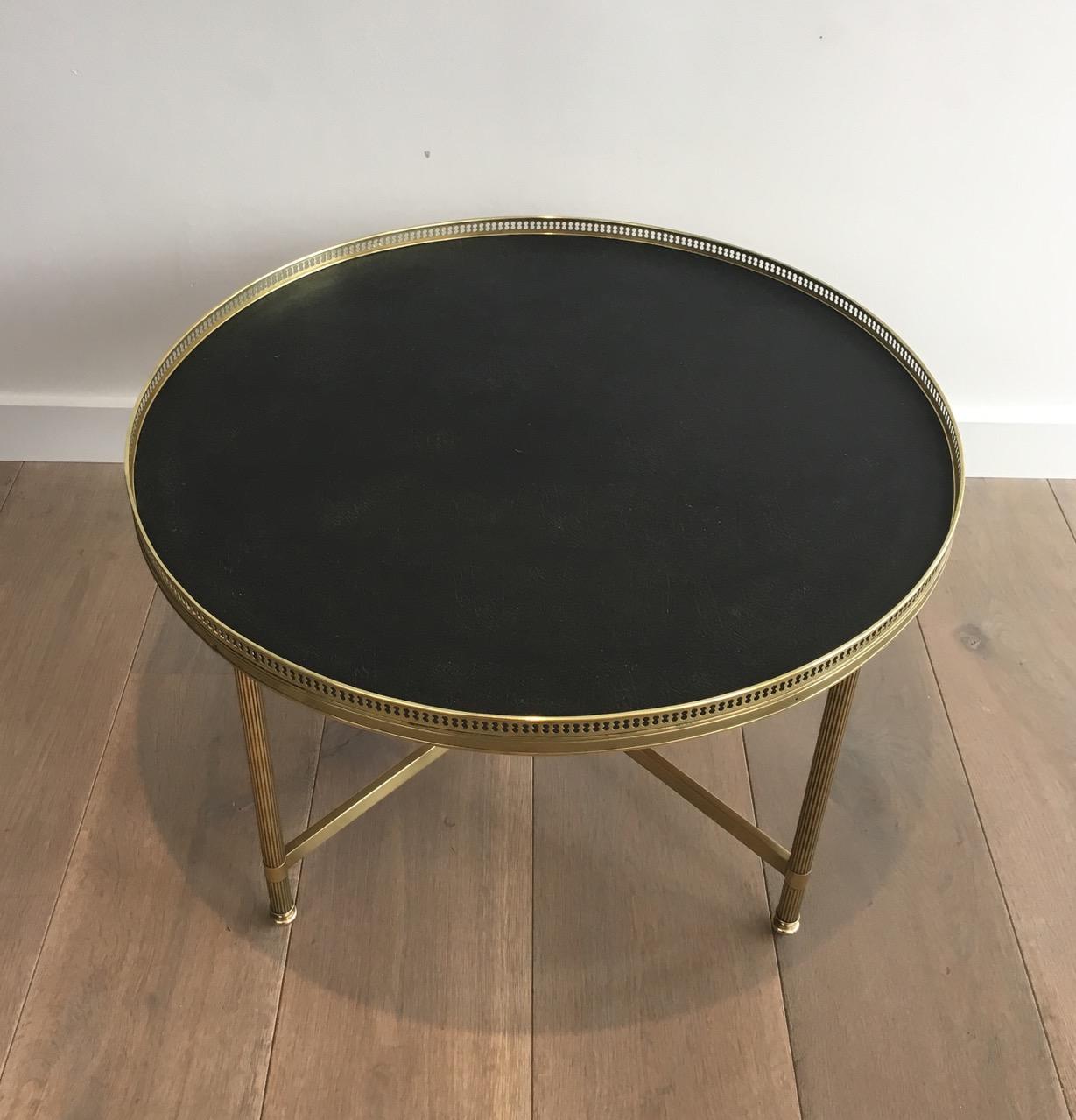 This neoclassical round coffee table is made of brass fluted legs, joined by a stretcher on which center is a nice ornament. The top is made of a faux leather surrounded by a fine brass gallery. 