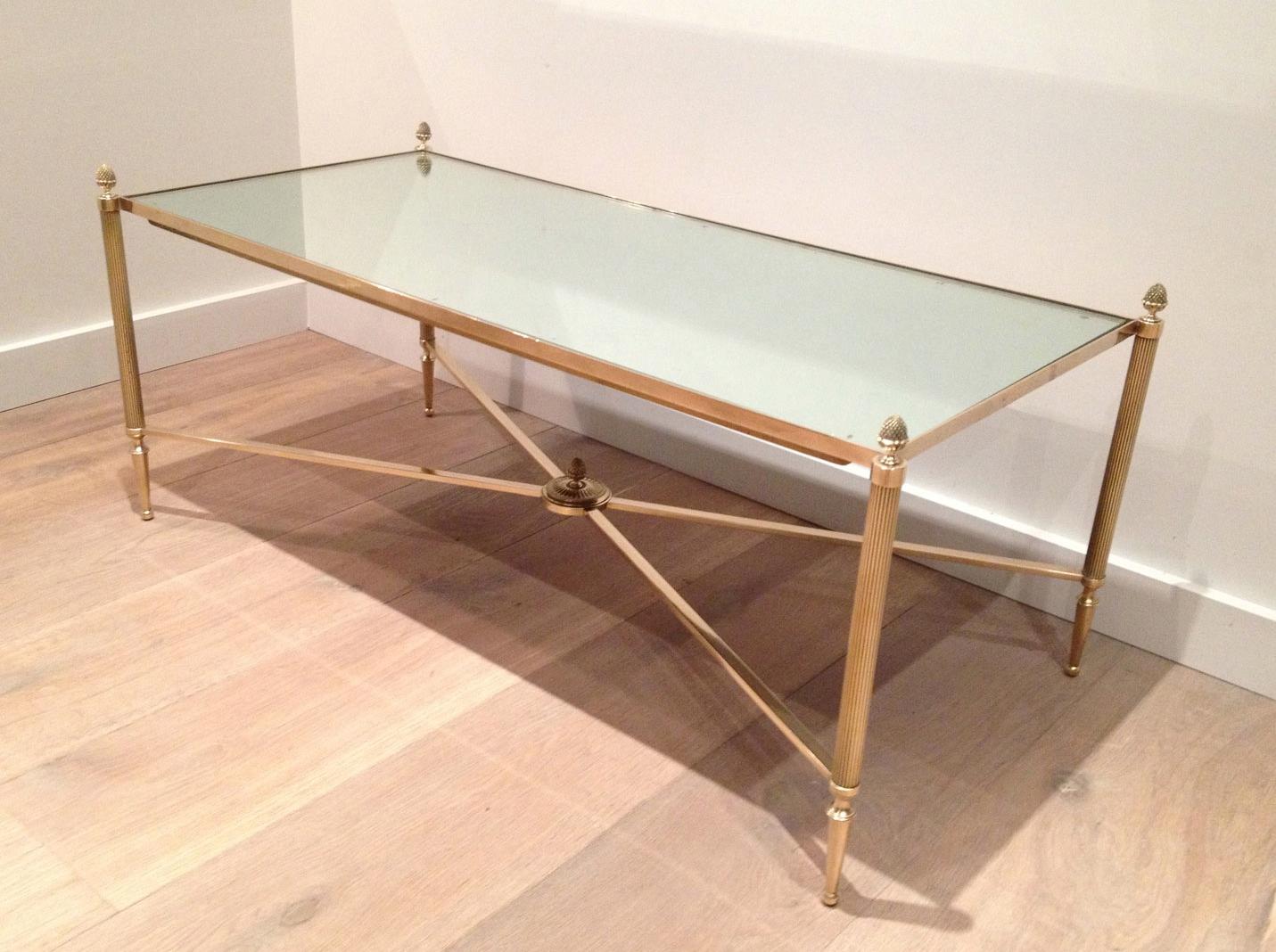 This elegant neoclassical style coffee table is all made of brass with a mirror shelf. This is a very nice cocktail table with a beautiful stretcher and fine finials on each corner. This coffee table was made by famous French designer Maison Baguès,