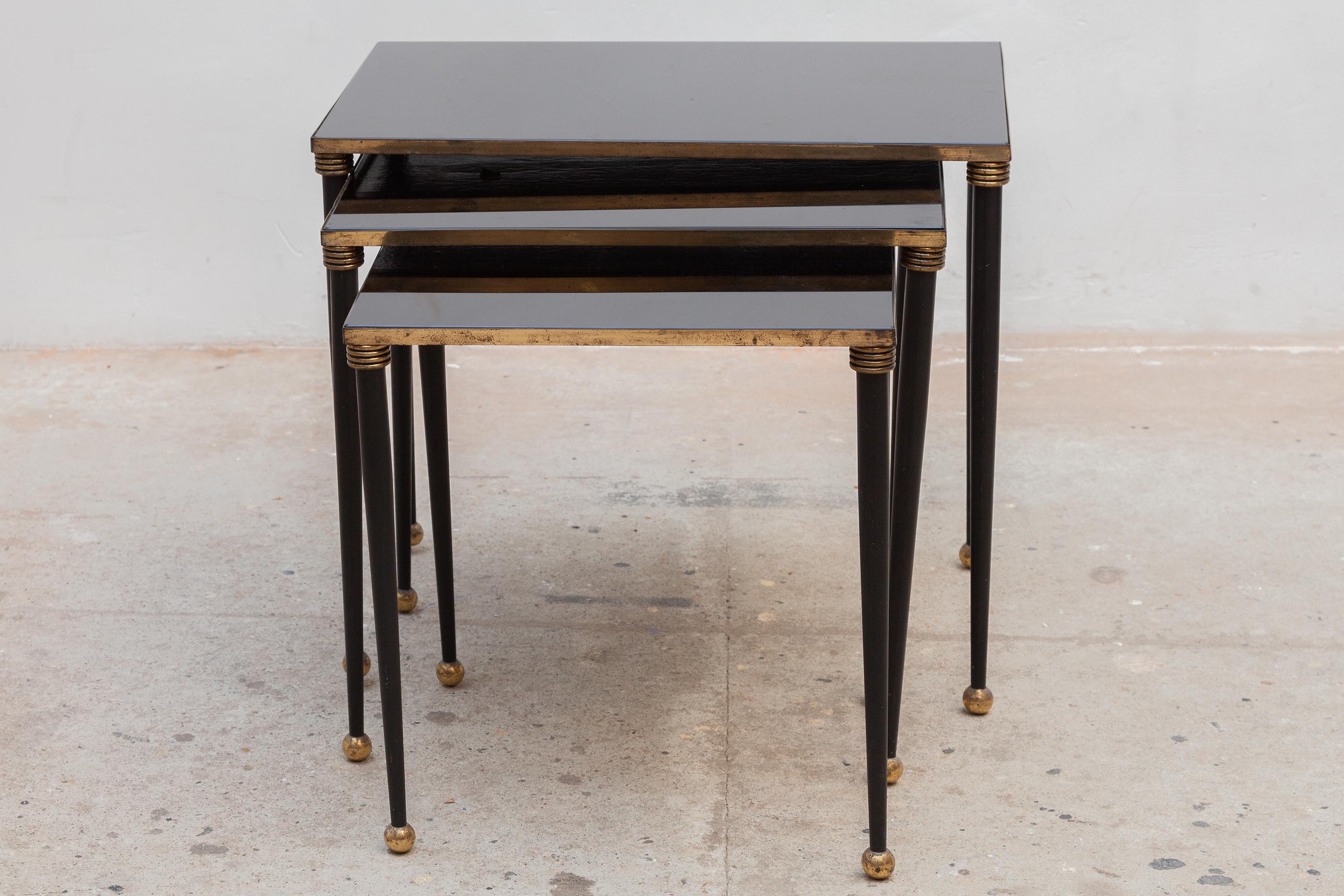 Vintage mid-century Maison Jansen nesting tables a trio with black metal frames with brass accents and black mirror tops, 1950`s ca, French.When stacked together these tables make an interesting geometric pattern.These tables are in good condition.