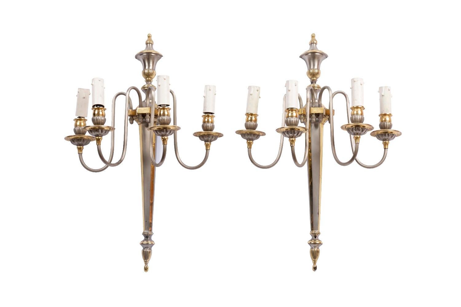 Maison Jansen, in the taste of.

Pair of Directoire style gilt and silver brass wall sconces with four arm lights. Chandelle shaft topped by an ancient covered vase and finished by a stylized motif of a reversed trimming tassel. The four arm