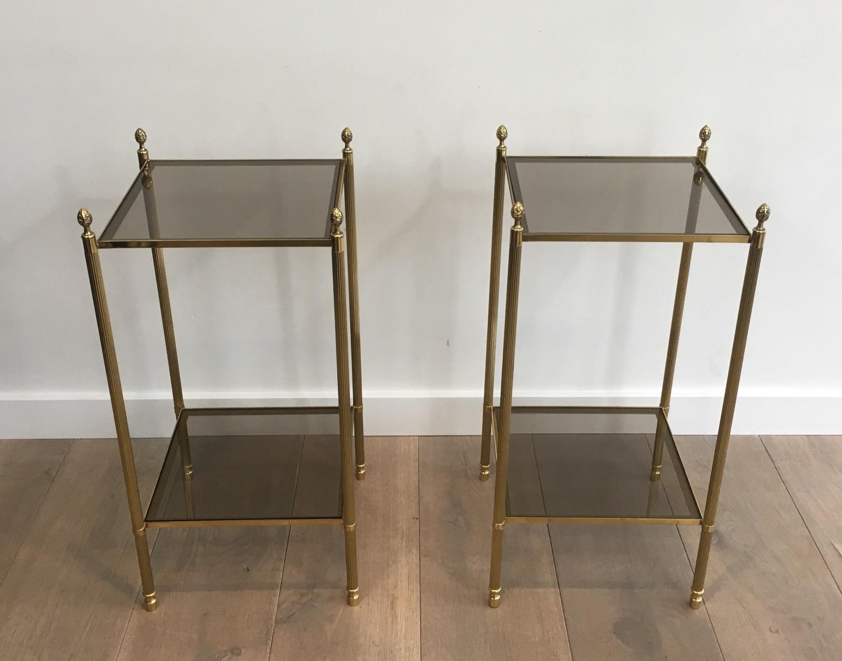 This nice pair of neoclassical style brass side tables is made of brass with smoked glass shelves (glass shelves can be changed for clear glass, mirror, faux-antiques mirror or black lacquered glass. This is a work by famous French designer Maison
