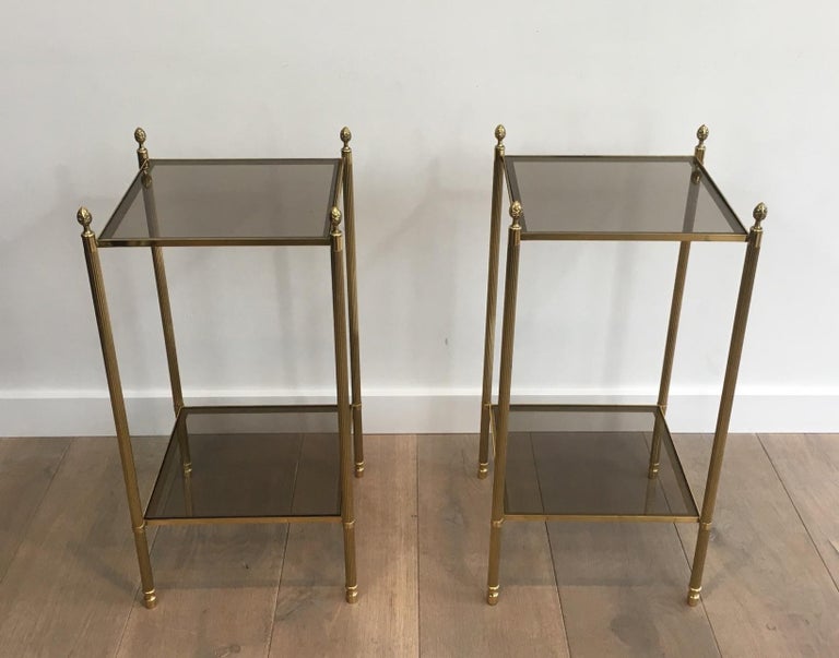 This nice pair of neoclassical style brass side tables is made of brass with smoked glass shelves (glass shelves can be changed for clear glass, mirror, faux-antiques mirror or black lacquered glass. This is a work by famous French designer Maison
