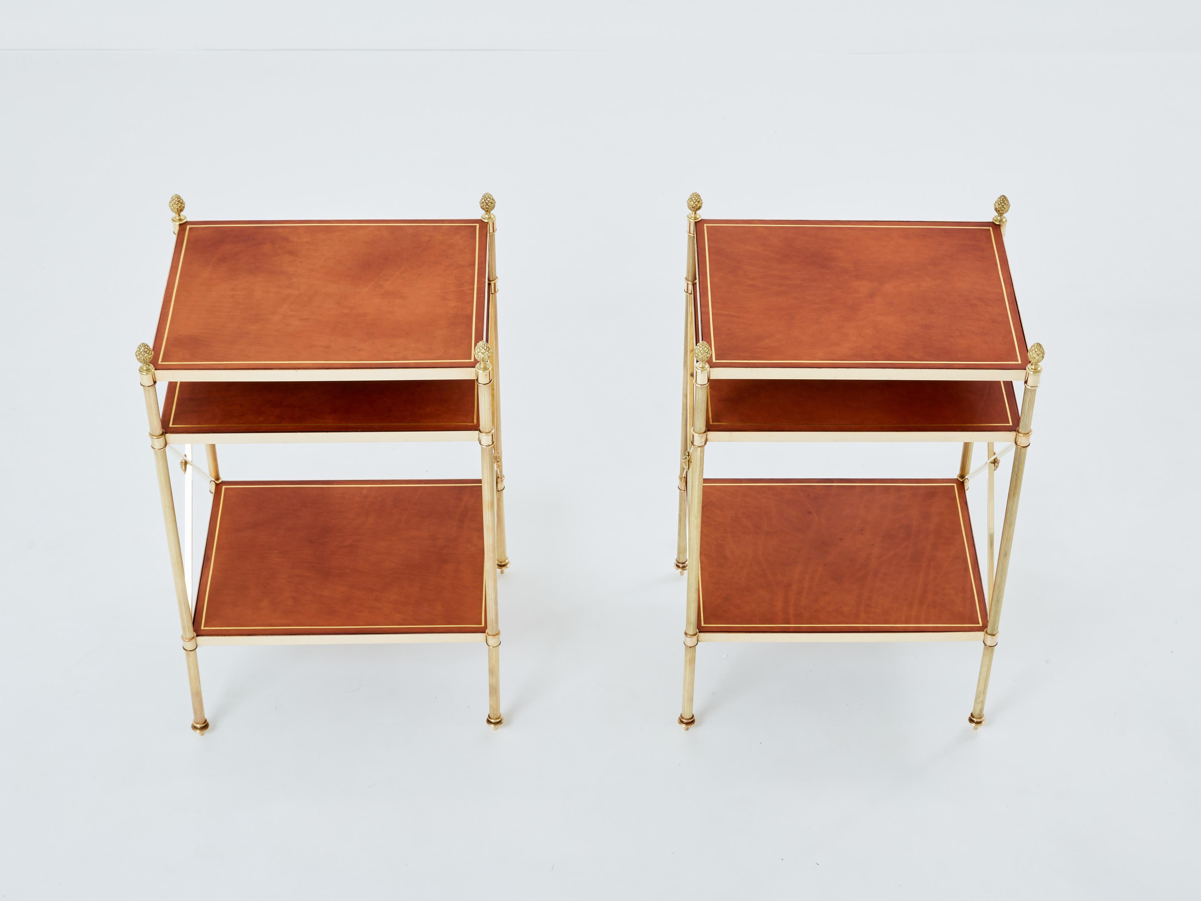 This beautiful pair of three-tier side tables by Maison Jansen was produced with solid brass and brown leather top in the early 1970s. Its crossed side with brass flowers, brass pine cones, and clean lines are typical of the French neoclassical work