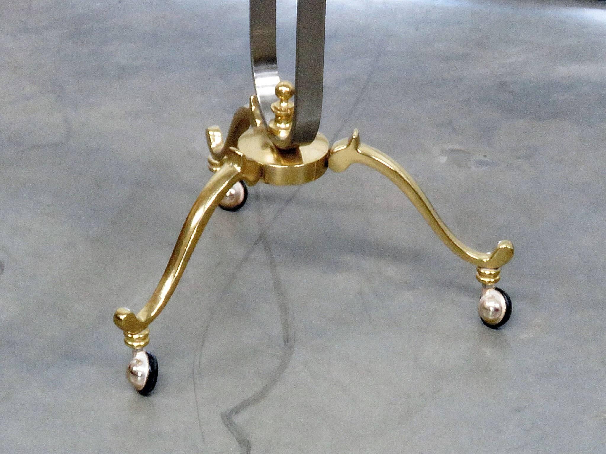 A Maison Jansen valet influenced by neoclassical themes with ram's head motif and produced in midcentury Italy. Consists of polished steel and accented in brass. The valet stands on tripod scroll form feet on casters, features a coin tray with