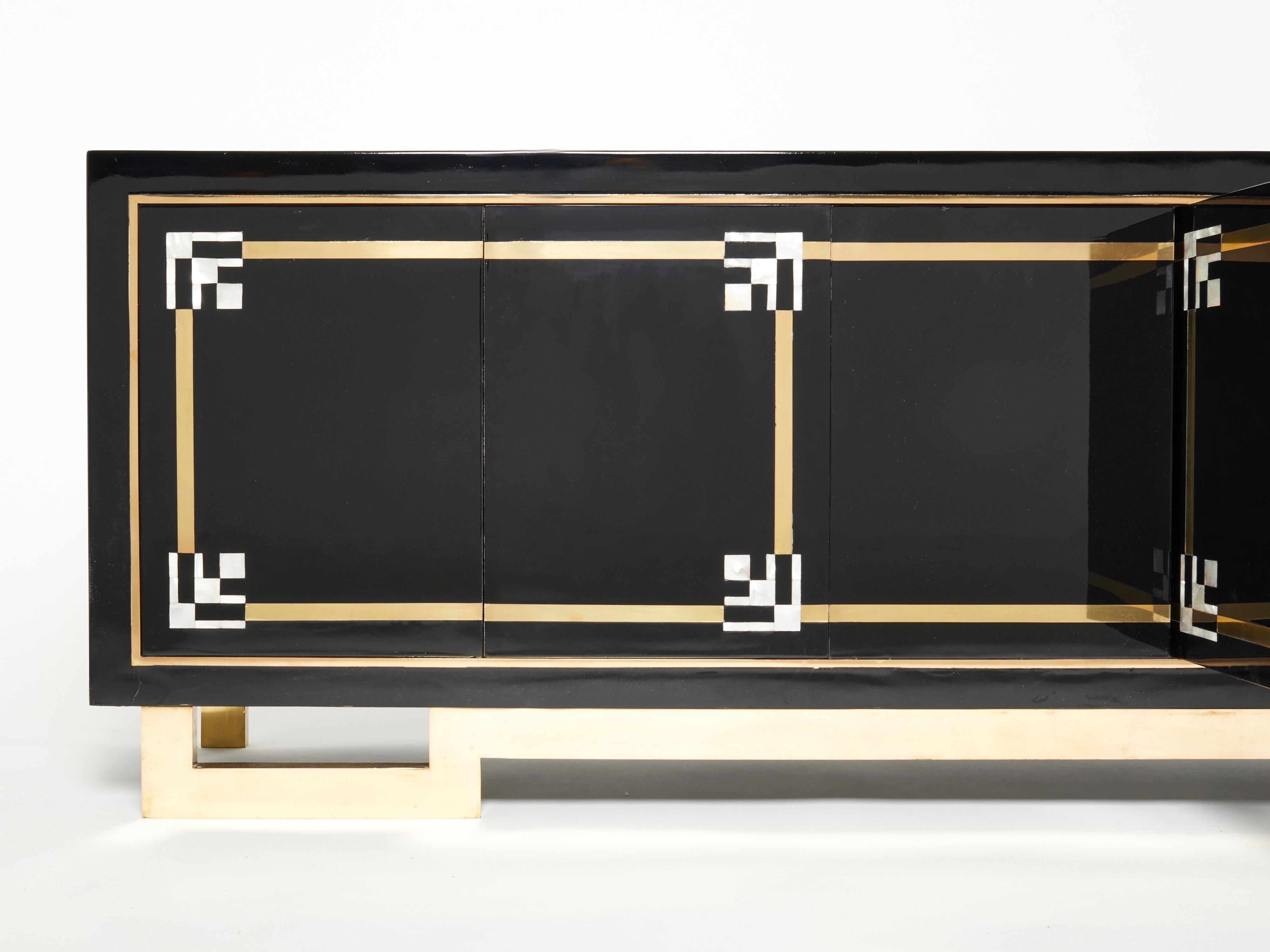 A unique and timeless vintage piece, this mid-century sideboard feels imposing and glamourous, with thick, straight lines of brass adorning its exterior of reflective black lacquer. Glossy black lacquer, paired with bright brass accents and shell