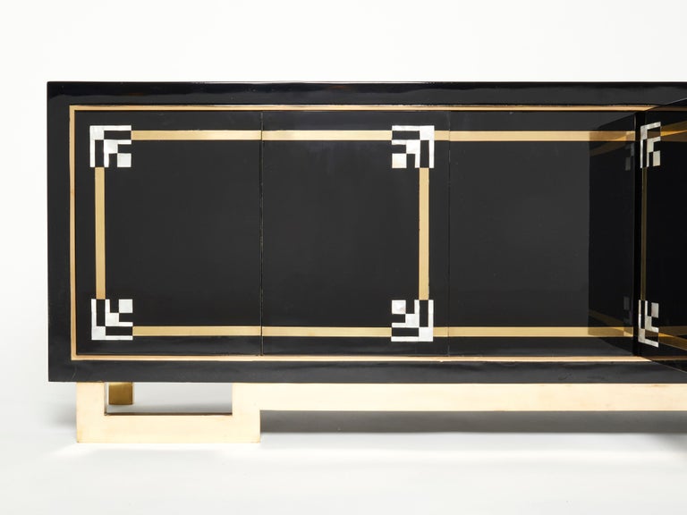 A unique and timeless vintage piece, this mid-century sideboard feels imposing and glamourous, with thick, straight lines of brass adorning its exterior of reflective black lacquer. Glossy black lacquer, paired with bright brass accents and shell