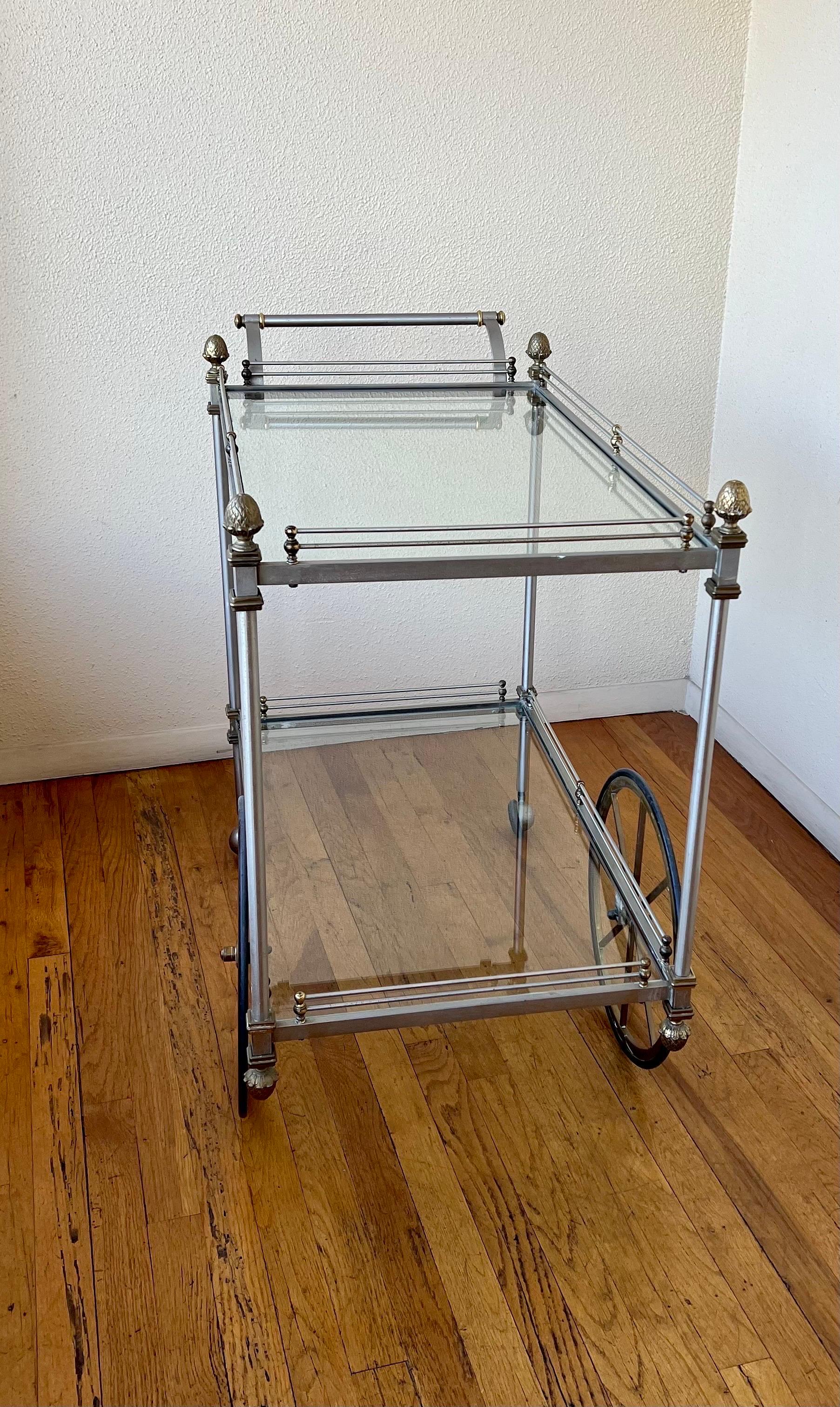 Maison Jansen two-tiered finely brushed steel and brass rolling bar cart trolley in overall beautifully aged original color patina. Campaign style that blends well with mid-century or Postmodern decor.